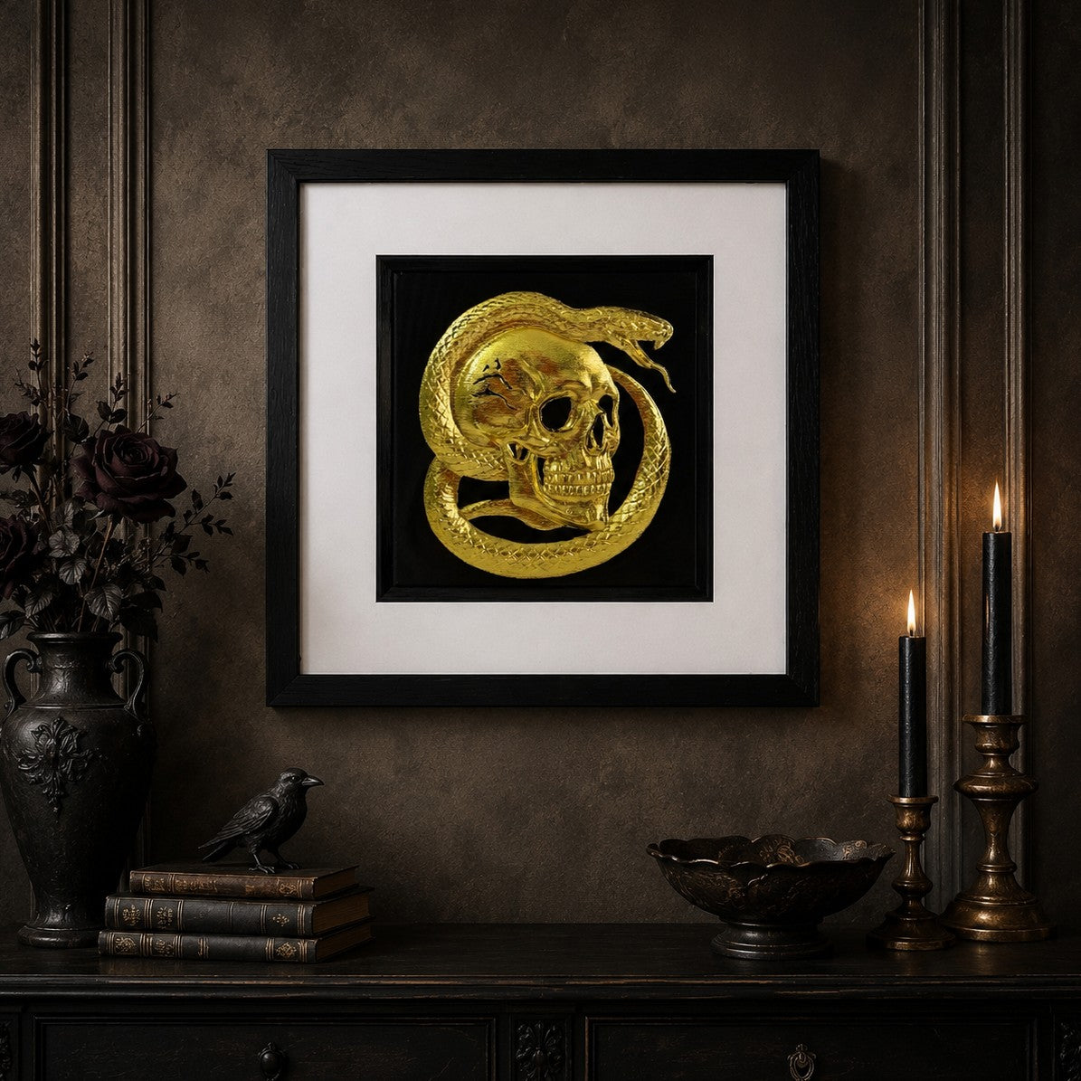 Framed gothic skull and serpent wall art with gold leaf design on a black background, styled in a dark candlelit interior with antique decor.
