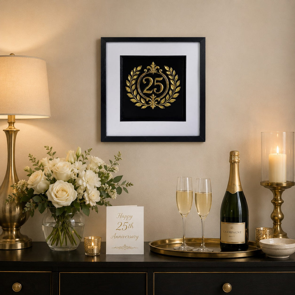Gold 25th anniversary laurel wreath framed artwork styled above a sideboard with flowers, champagne, candles, and an anniversary card.