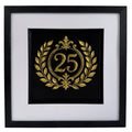 Straight-on Gold 25th anniversary laurel wreath framed artwork with raised number 25, black background, white mount, and black frame.