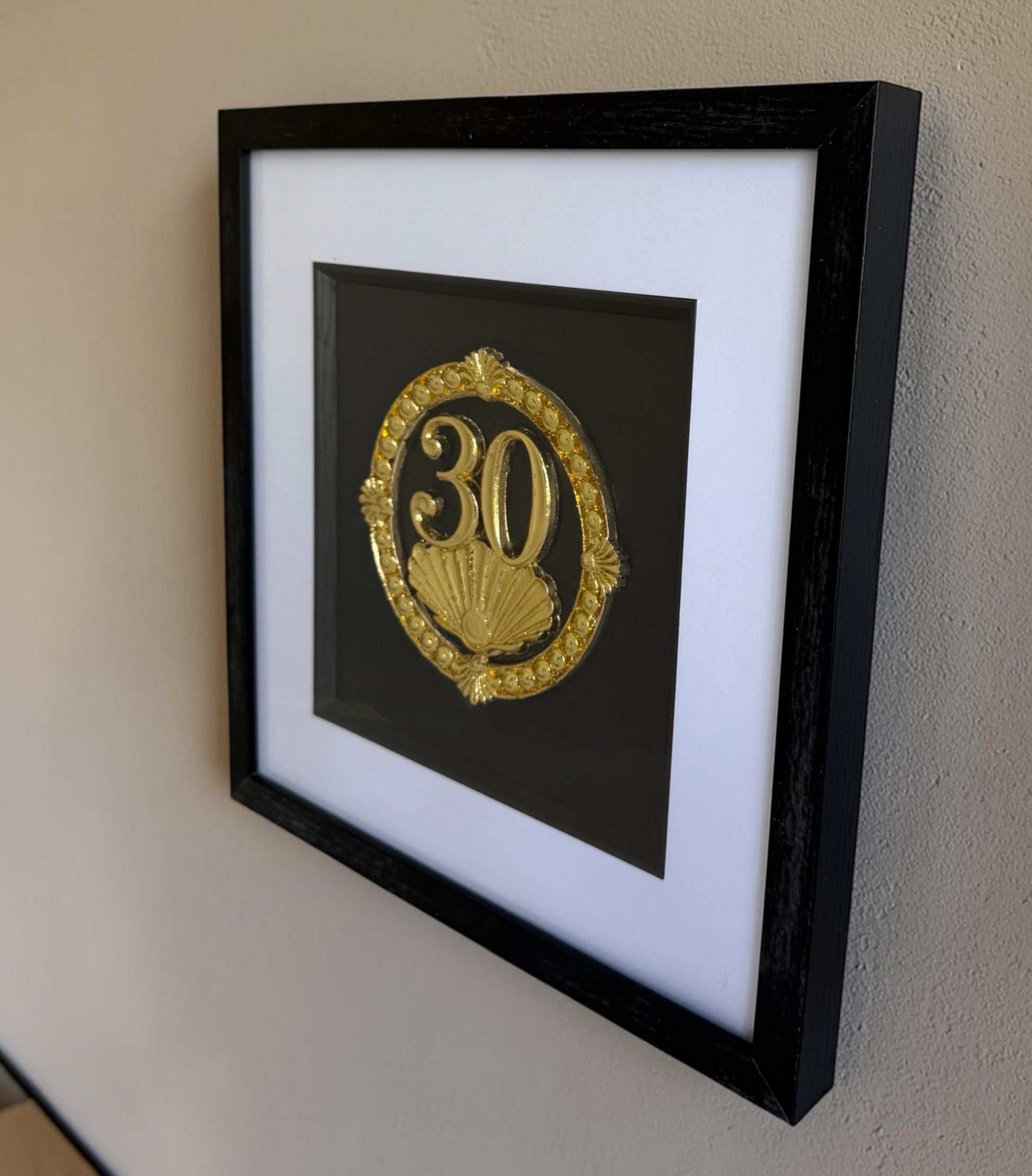 Gold framed 30th anniversary pearl shell artwork hanging on a wall, showing the raised number 30, black box frame, white mount, and glass front.