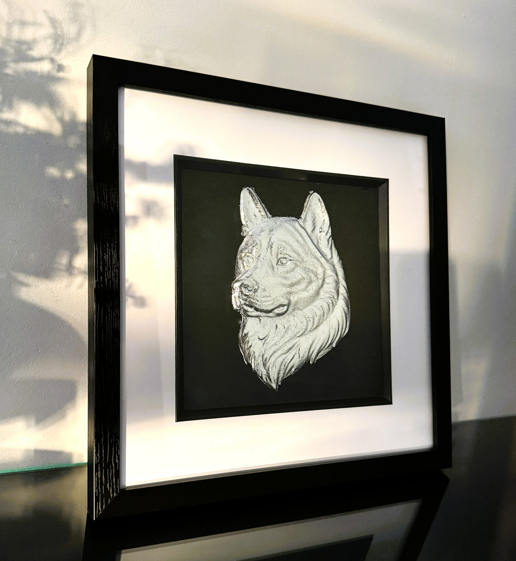 Angled view of framed Akita wall art in silver leaf showing raised Akita dog head relief with soft natural light and gallery style framing