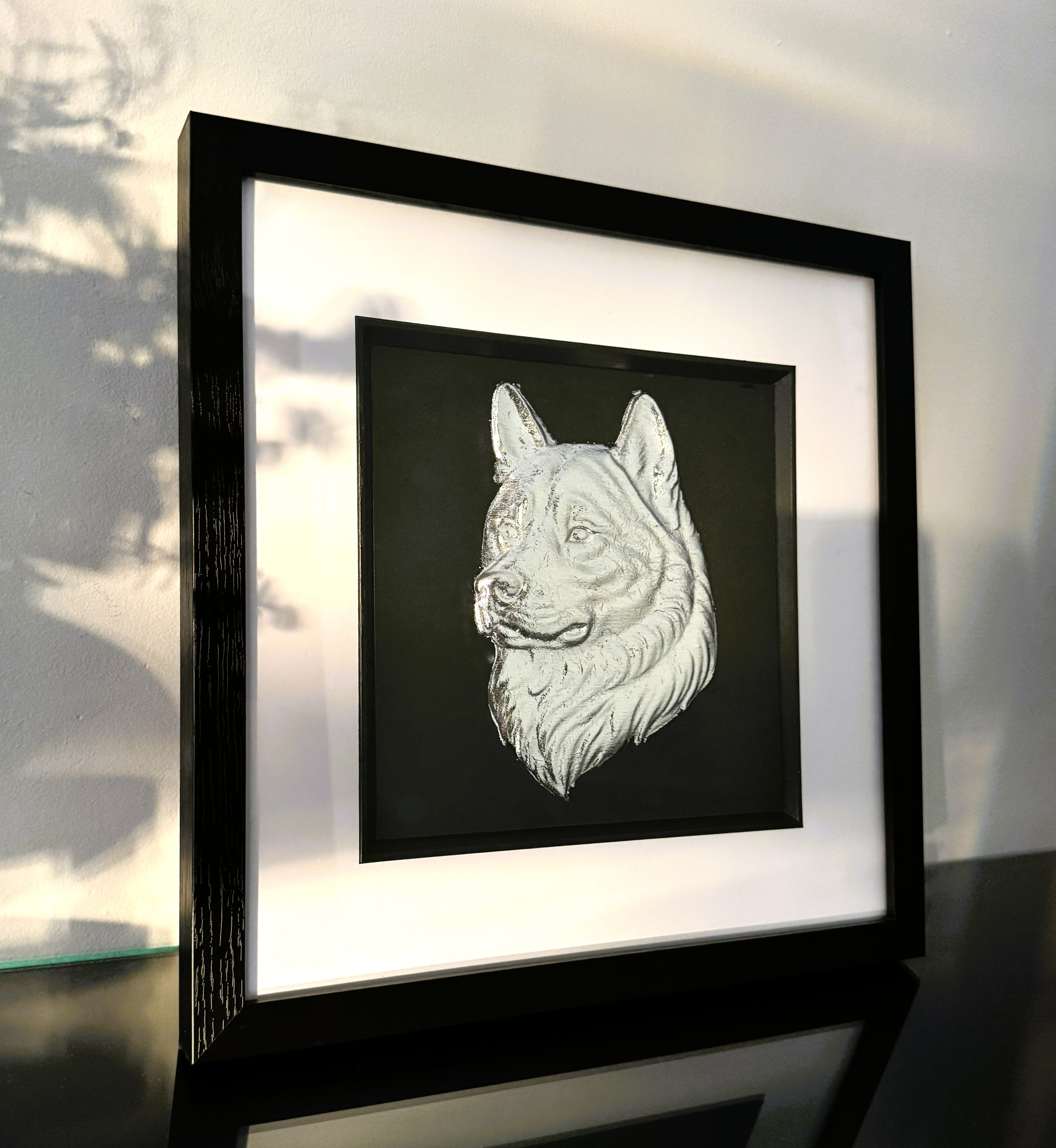 Angled view of framed Akita wall art in silver leaf showing raised Akita dog head relief with soft natural light and gallery style framing