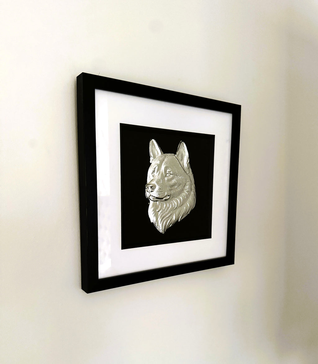Wall-mounted Akita wall art in silver leaf displayed in a black frame with white mount, showing a sculpted Akita dog head relief against a black background