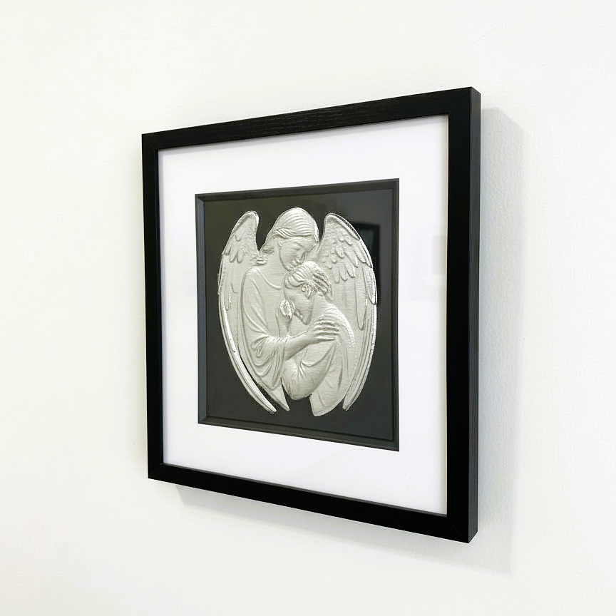 Angel holding person wall art mounted on a light wall, framed in black with white mount