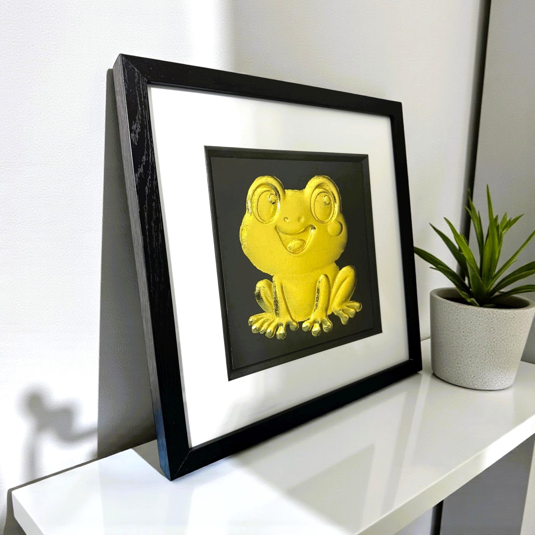 Kawaii frog gold leaf framed wall art on black background on a desk