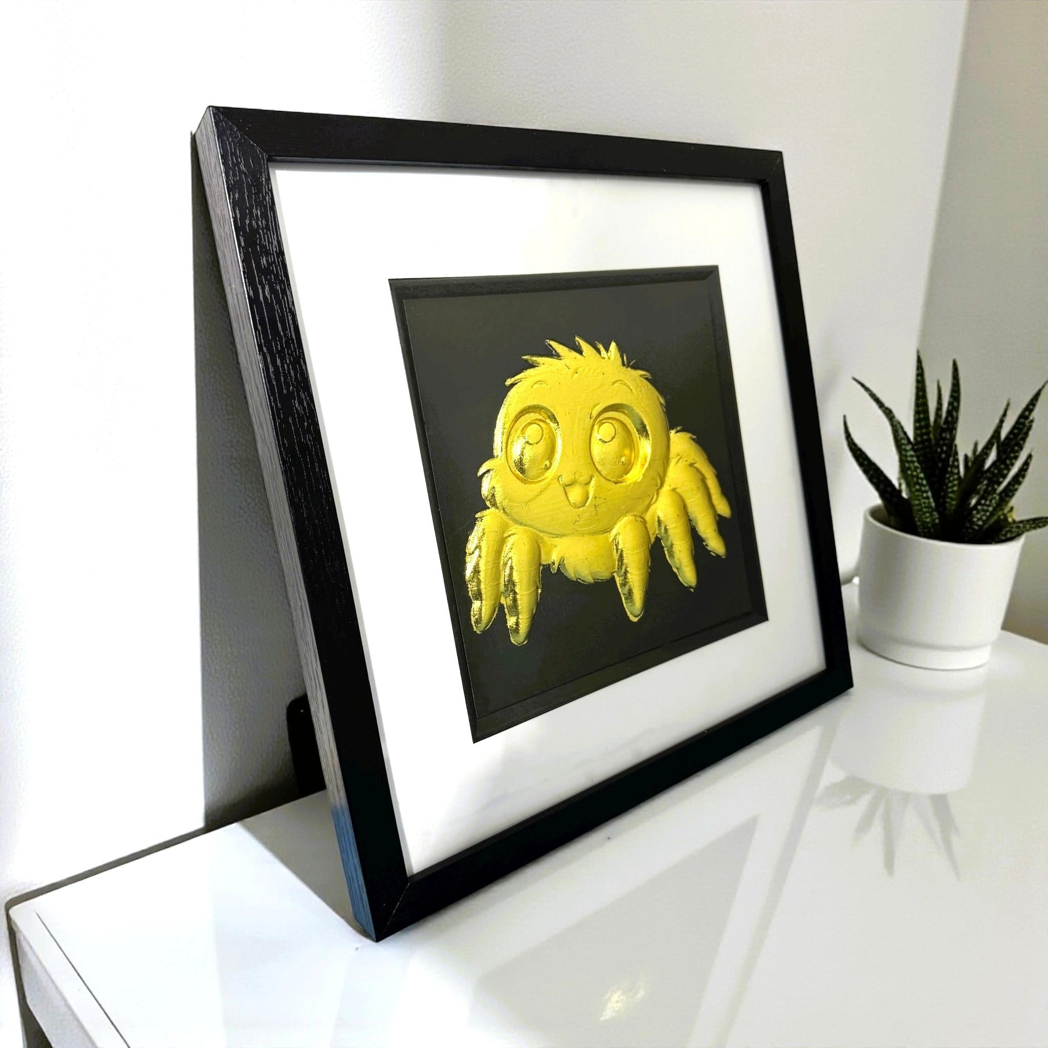 Angled desk view of Gold jumping spider wall art in a black frame with black background