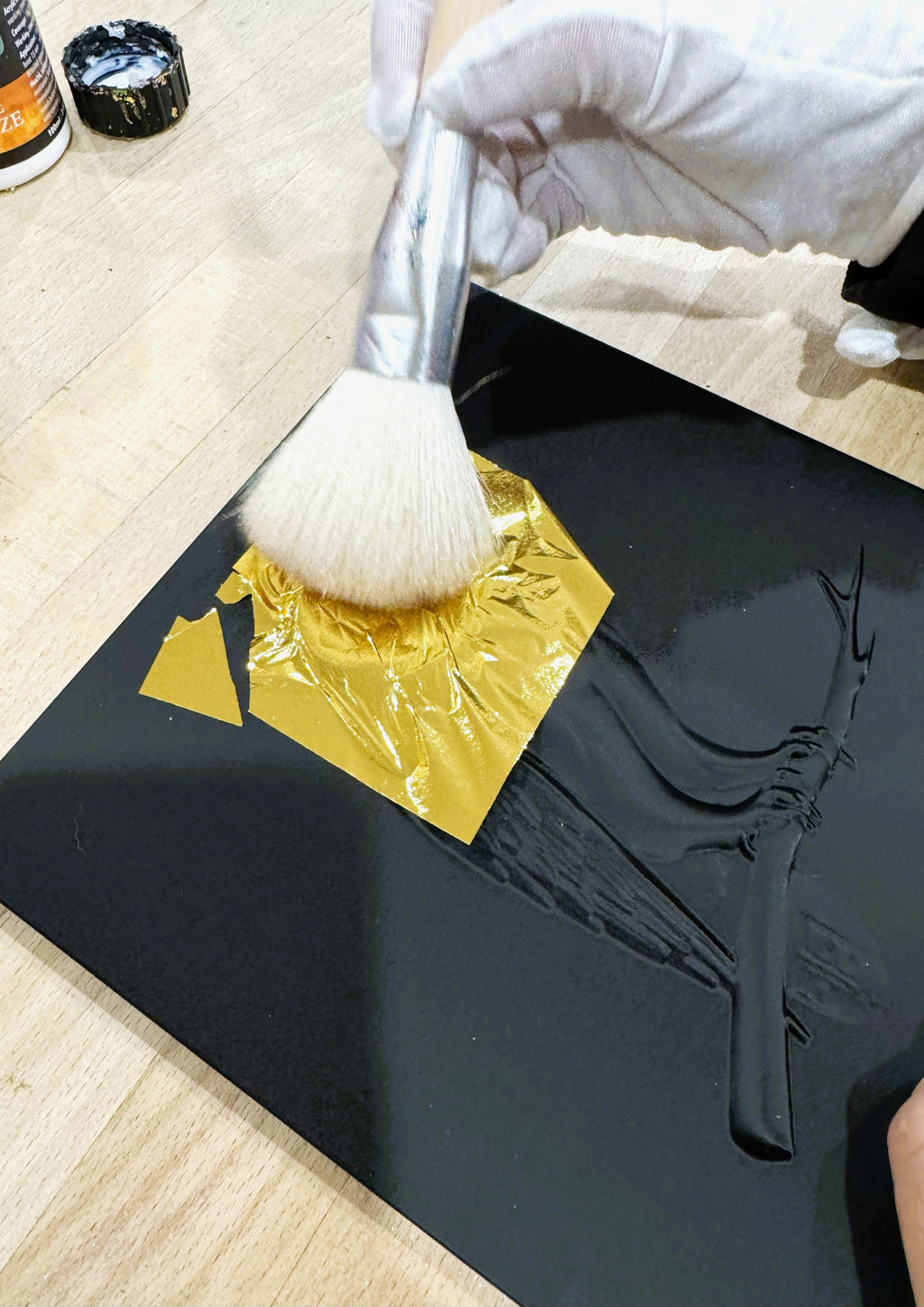 Applying gold leaf by hand to raised relief wall art using a soft brush