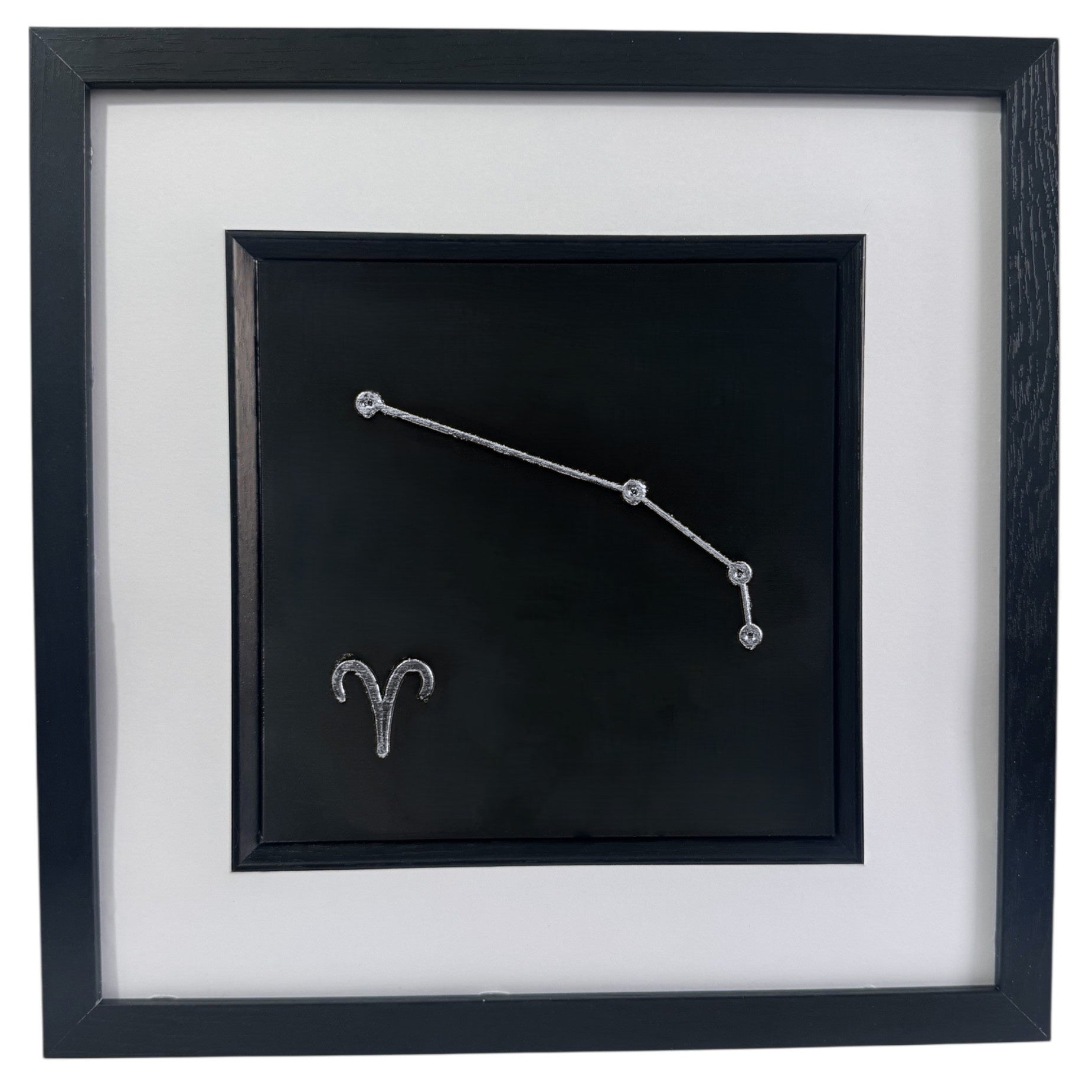 Framed Aries constellation wall art in silver leaf with star pattern and zodiac symbol, centred on a black background with white mount and black frame