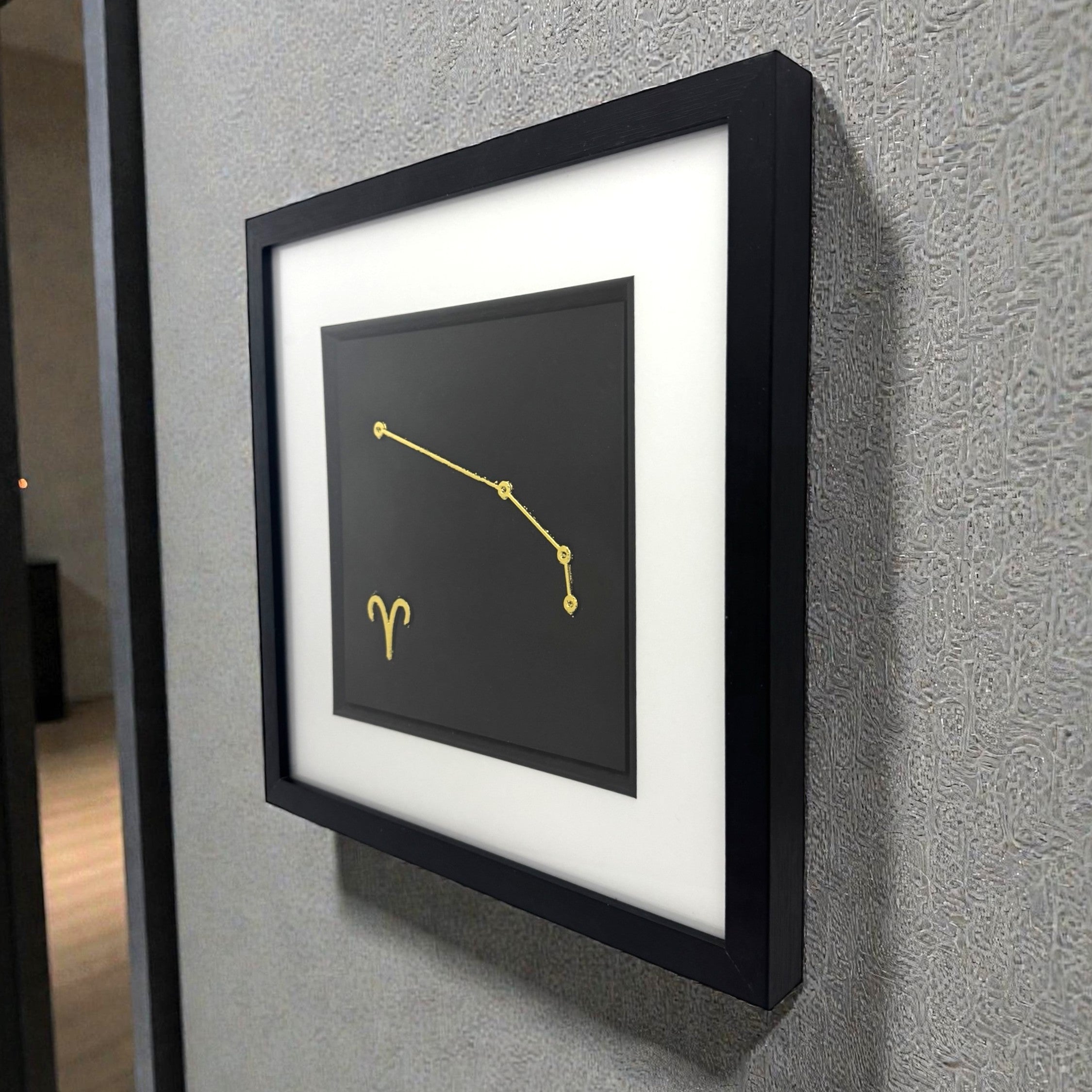 Framed Aries constellation wall art in gold leaf mounted on a wall, shown at an angle highlighting the depth and clean presentation