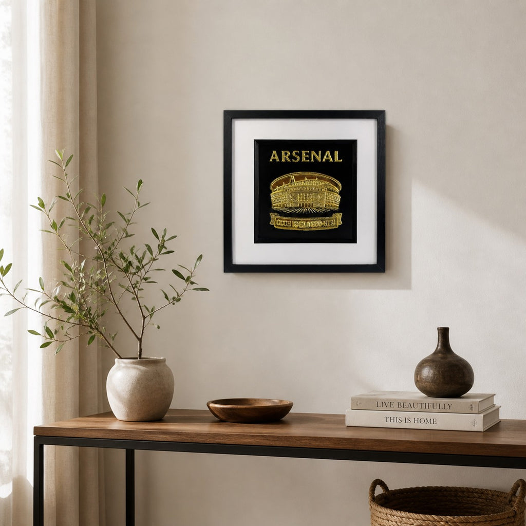 Gold Arsenal Emirates Stadium wall art in a black square frame with white mount, displayed on a neutral wall above a wooden console table.
