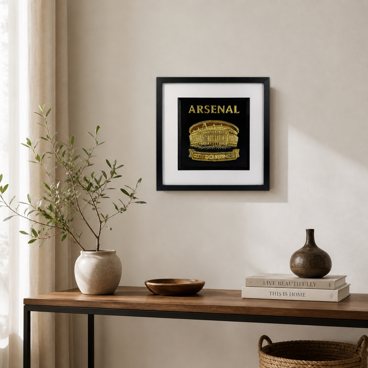 Gold Arsenal Emirates Stadium wall art in a black square frame with white mount, displayed on a neutral wall above a wooden console table.