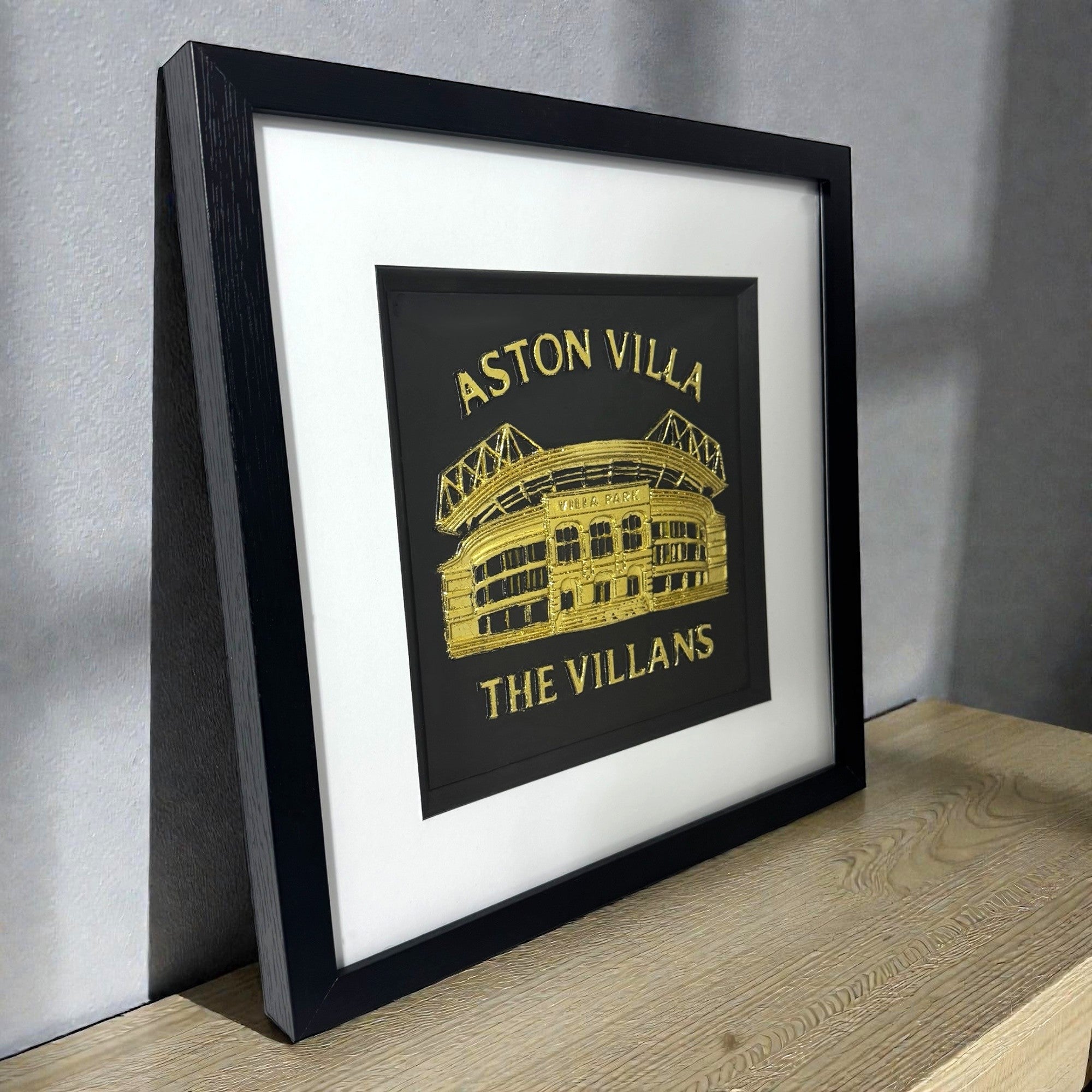 Angled view of gold leaf Aston Villa stadium wall art showing frame depth, raised architectural relief, and metallic highlights
