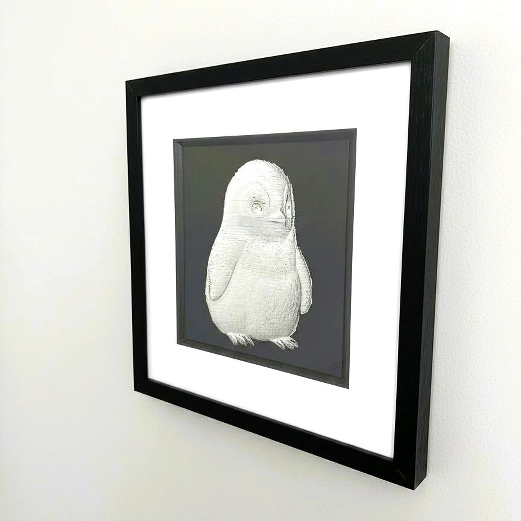 Silver baby penguin wall art framed in black hanging on a wall