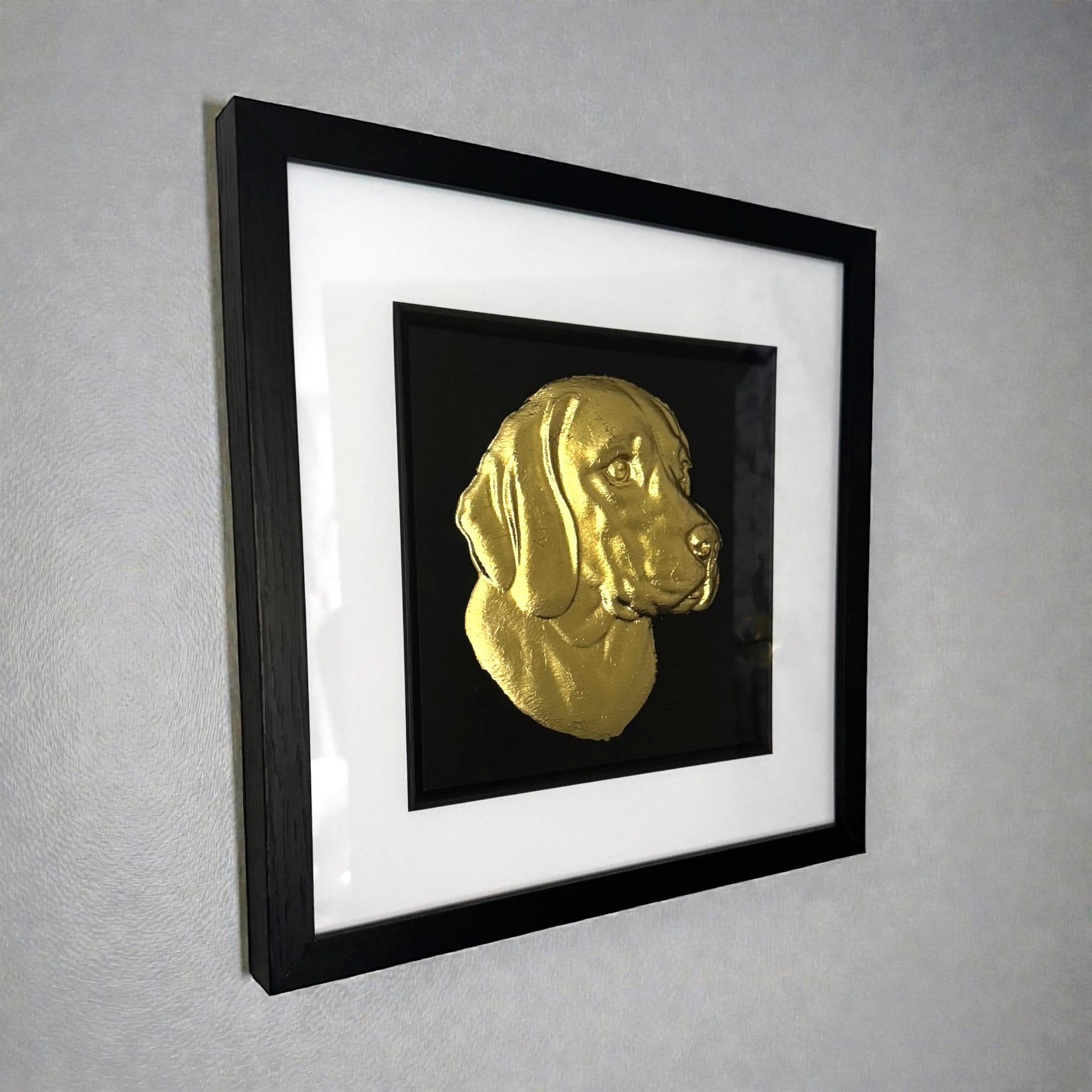 Framed beagle wall art featuring a gold relief portrait on a black background, shown hanging on a light grey wall with a black frame and white mount