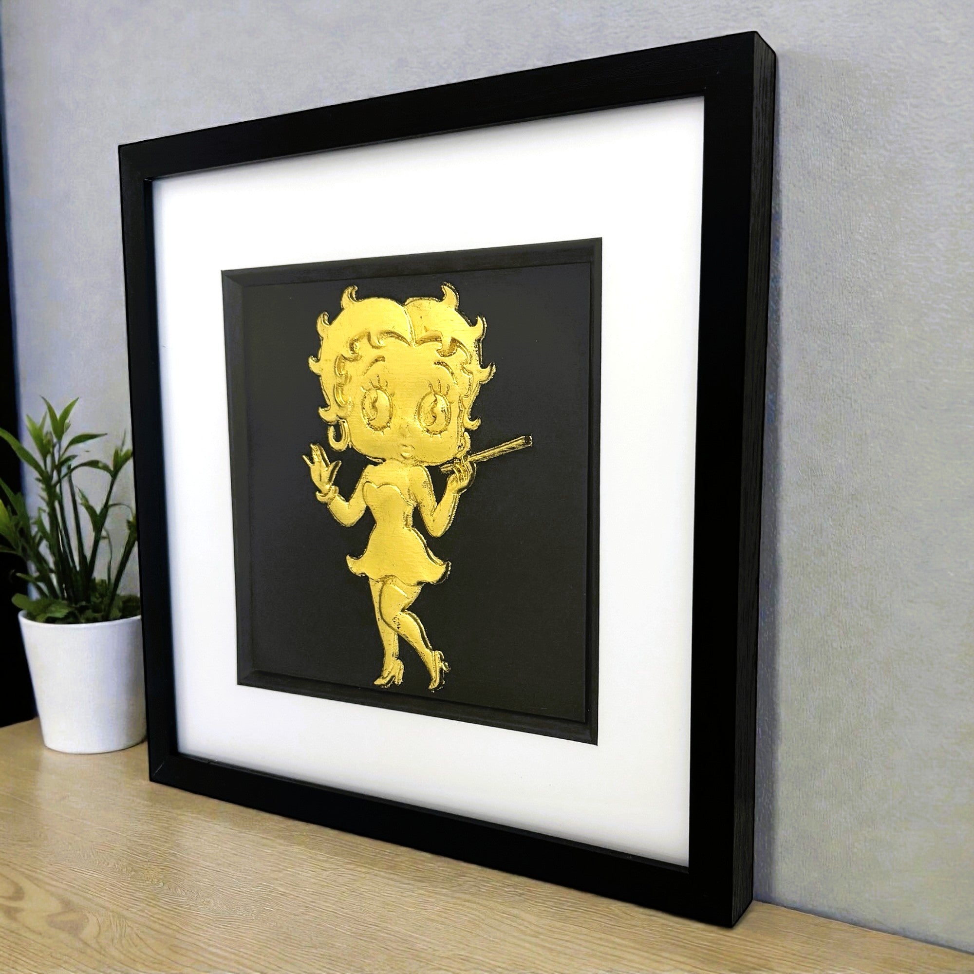 Gold leaf vintage cartoon figure wall art with white mount and black background on desk