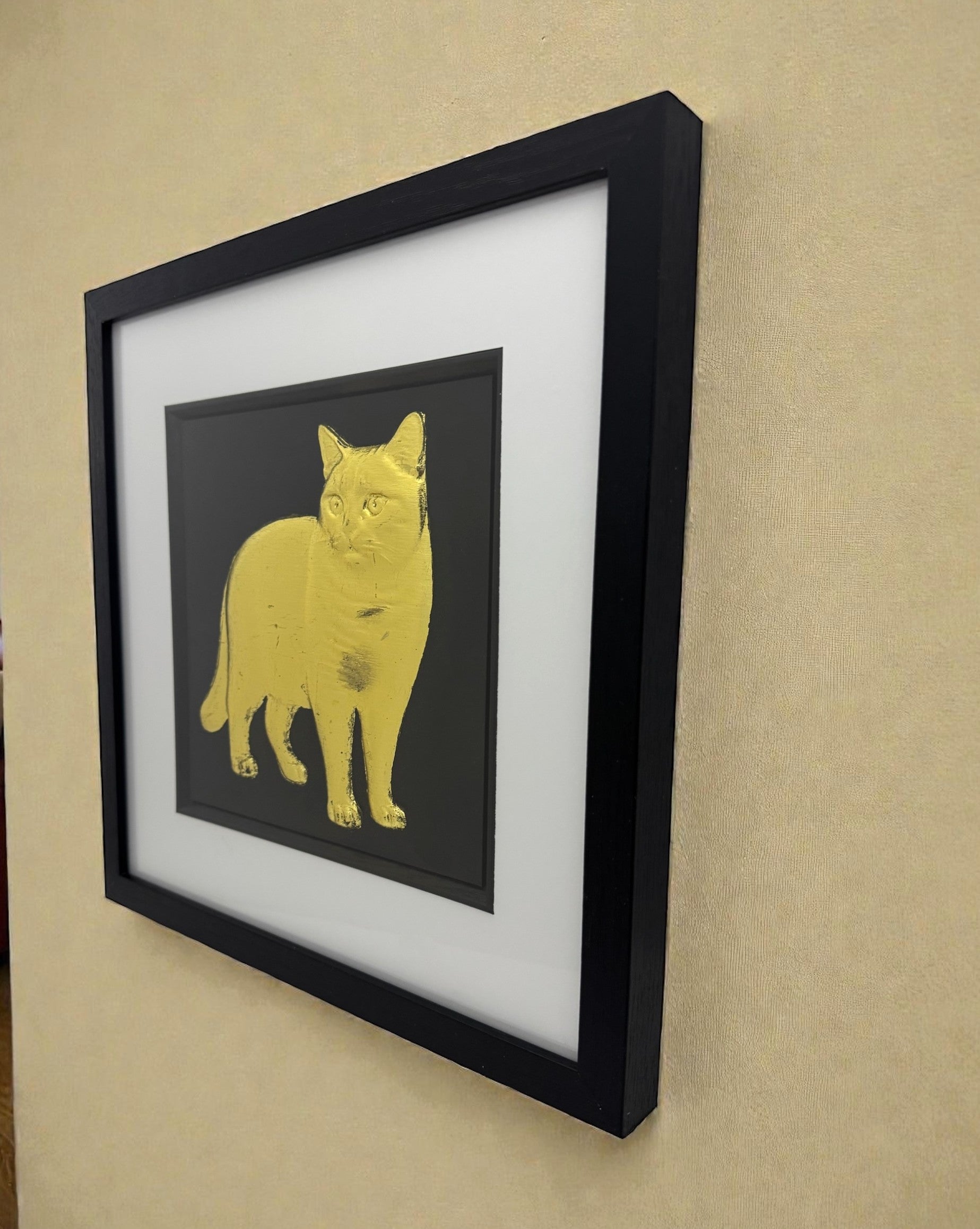 British Shorthair cat wall art in gold leaf 3D relief, framed in black box frame with white mount and glass front, angled wall view