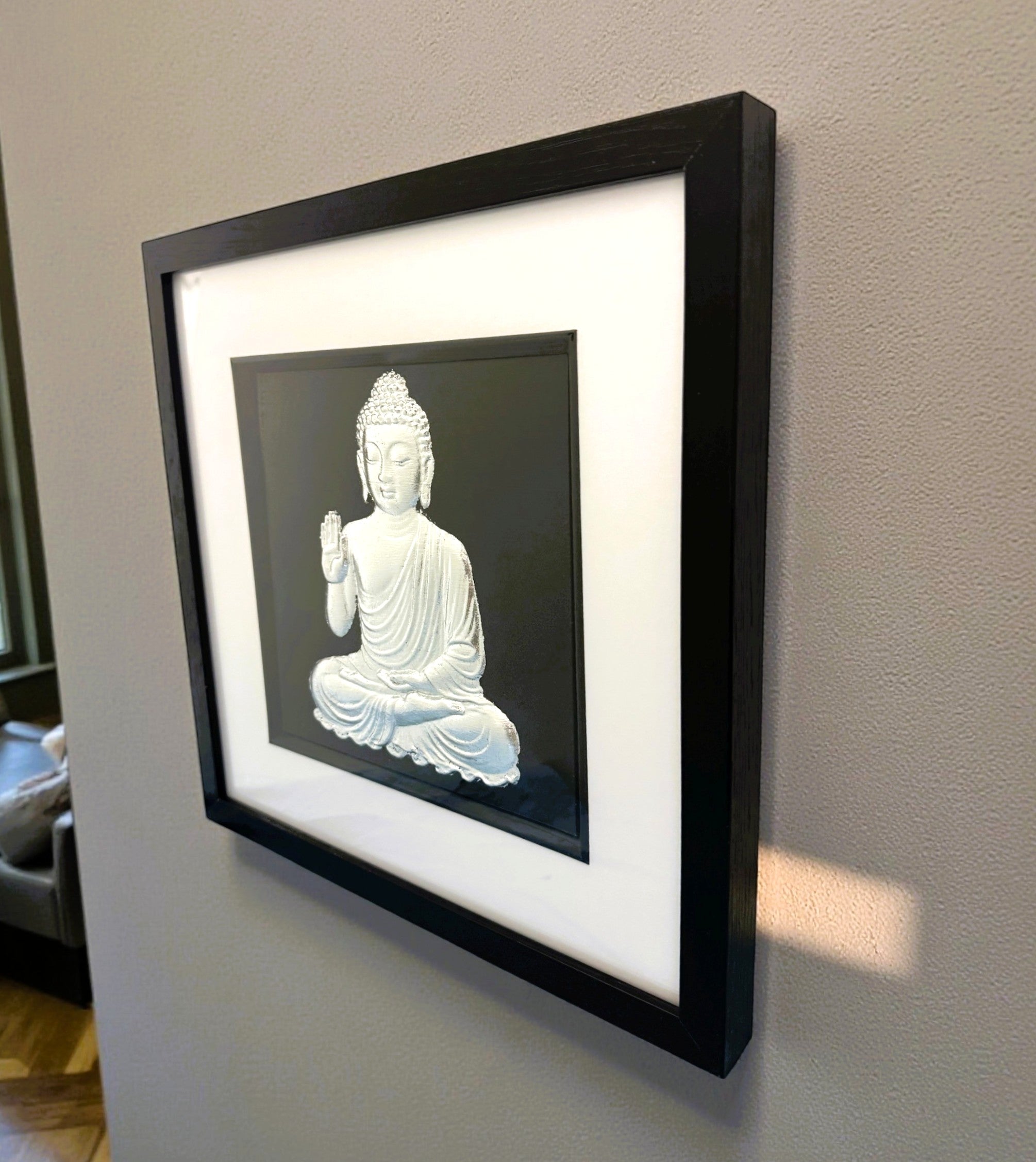 Wall-mounted silver leaf Buddha wall art framed in black on a neutral wall