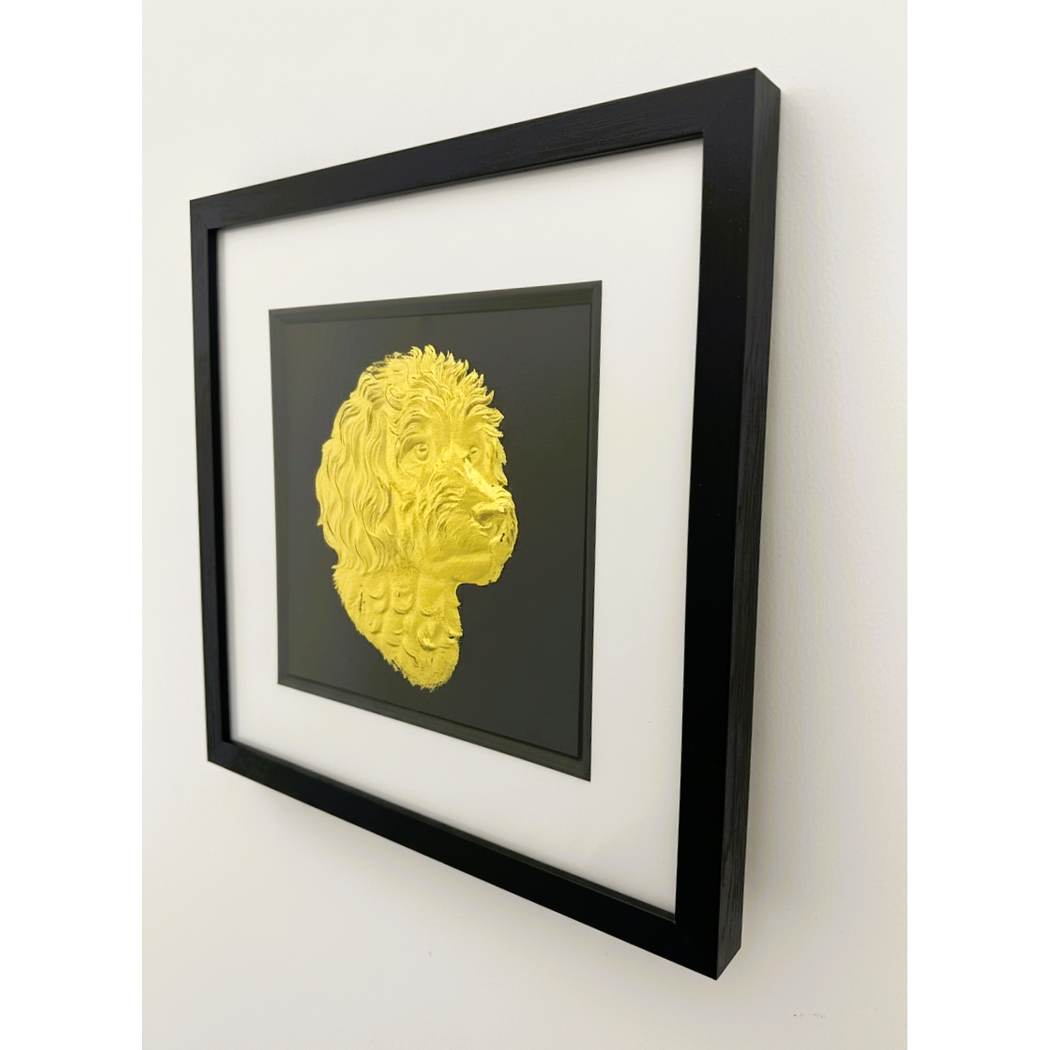 Framed cavapoo wall art featuring a gold relief portrait on a black background, shown hanging on a light wall in a black frame with white mount