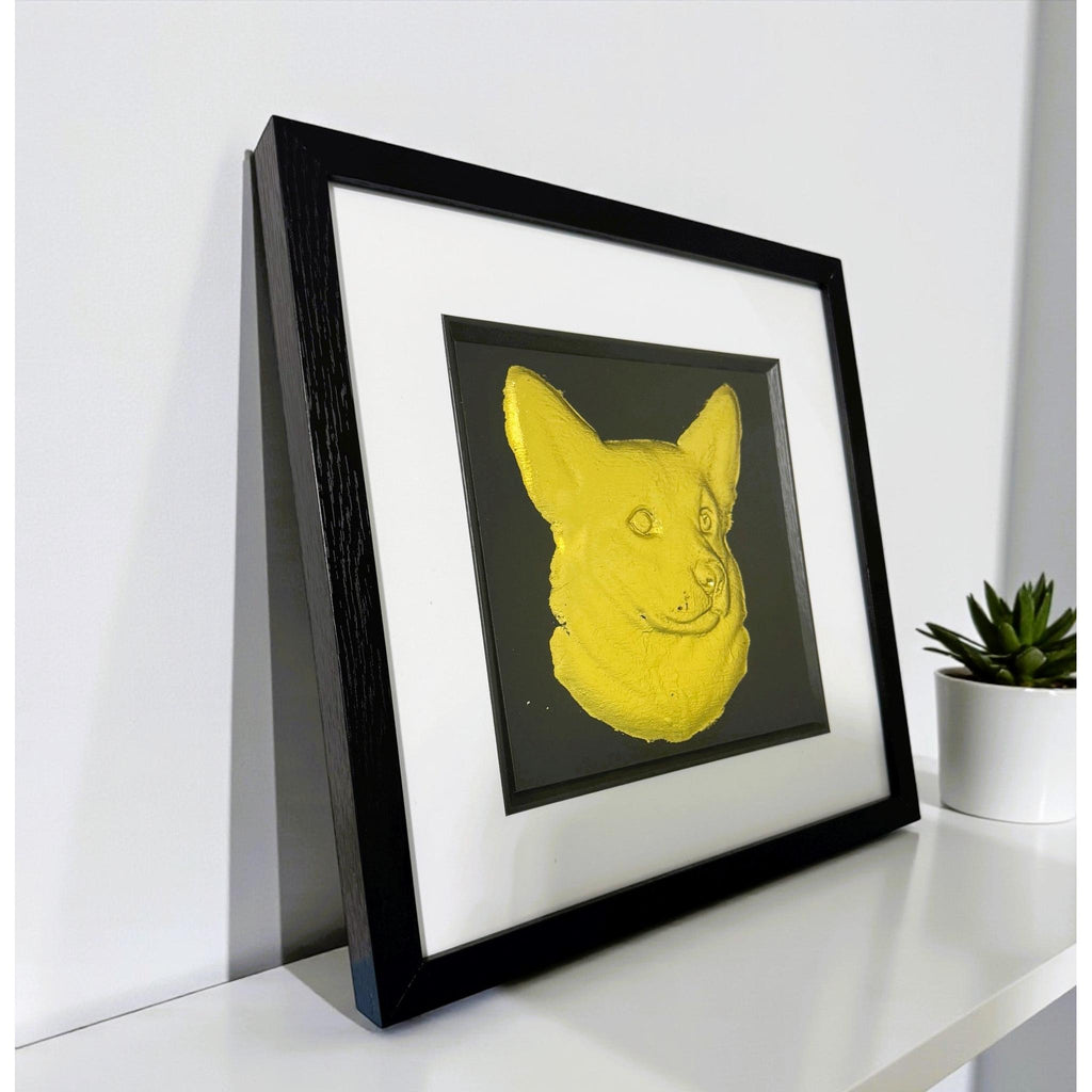 Framed corgi wall art featuring a gold relief portrait on a black background, shown angled on a white shelf with a small plant for scale