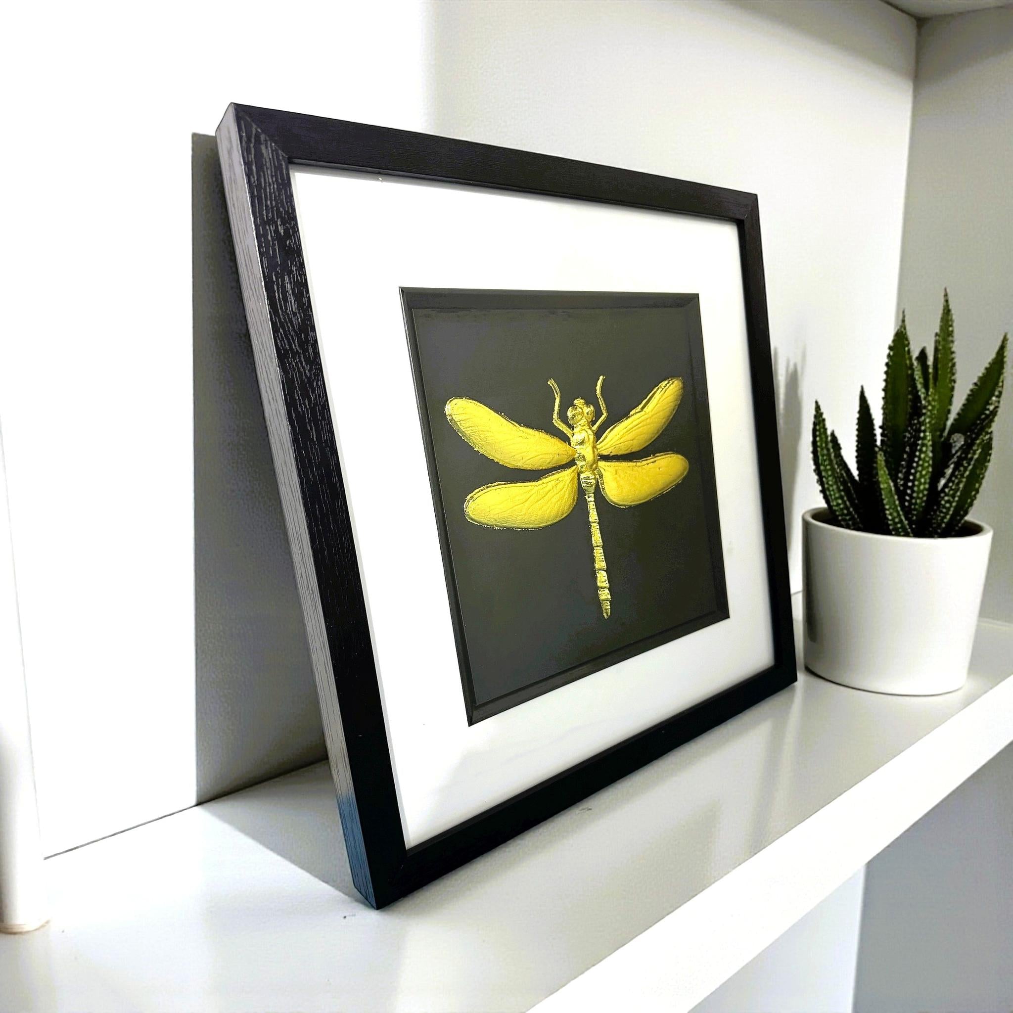 Angled view of gold leaf dragonfly framed artwork displayed on a shelf