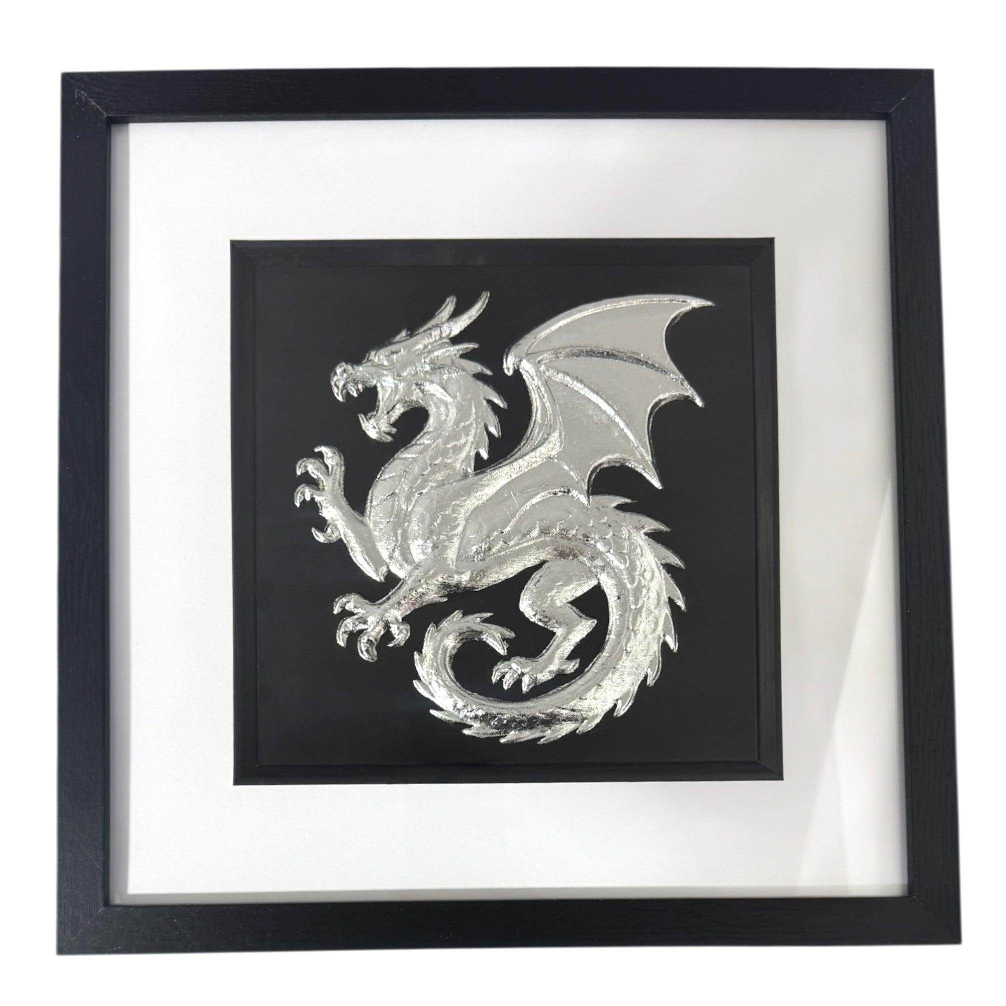 Framed dragon wall art in silver leaf relief, centred on a black background with white mount and black frame