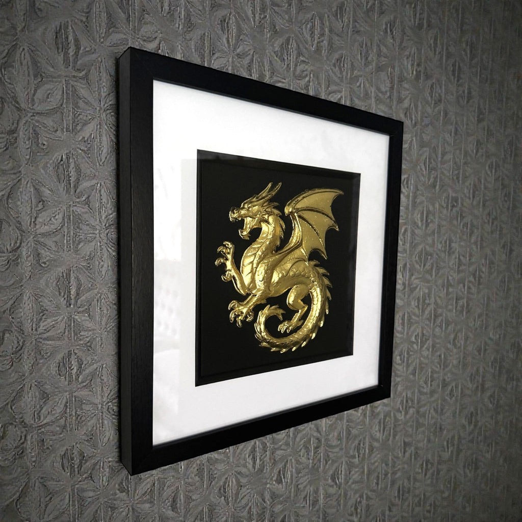 Framed dragon wall art in gold leaf relief mounted on a wall, shown at an angle highlighting depth and texture