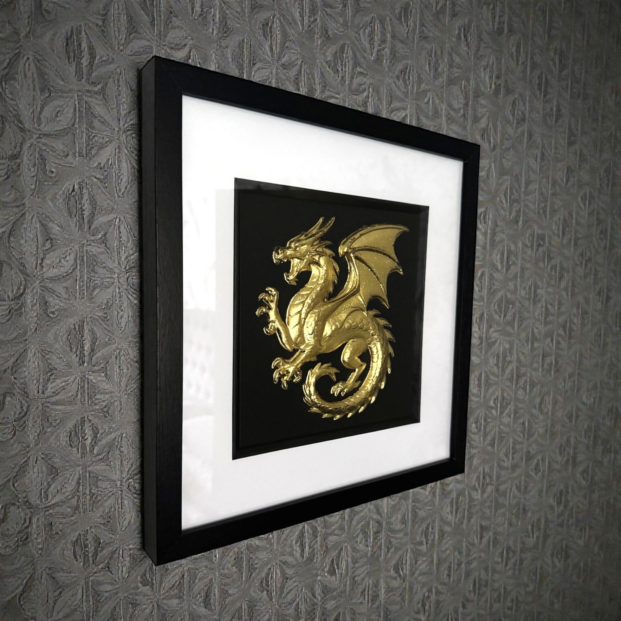 Framed dragon wall art in gold leaf relief mounted on a wall, shown at an angle highlighting depth and texture