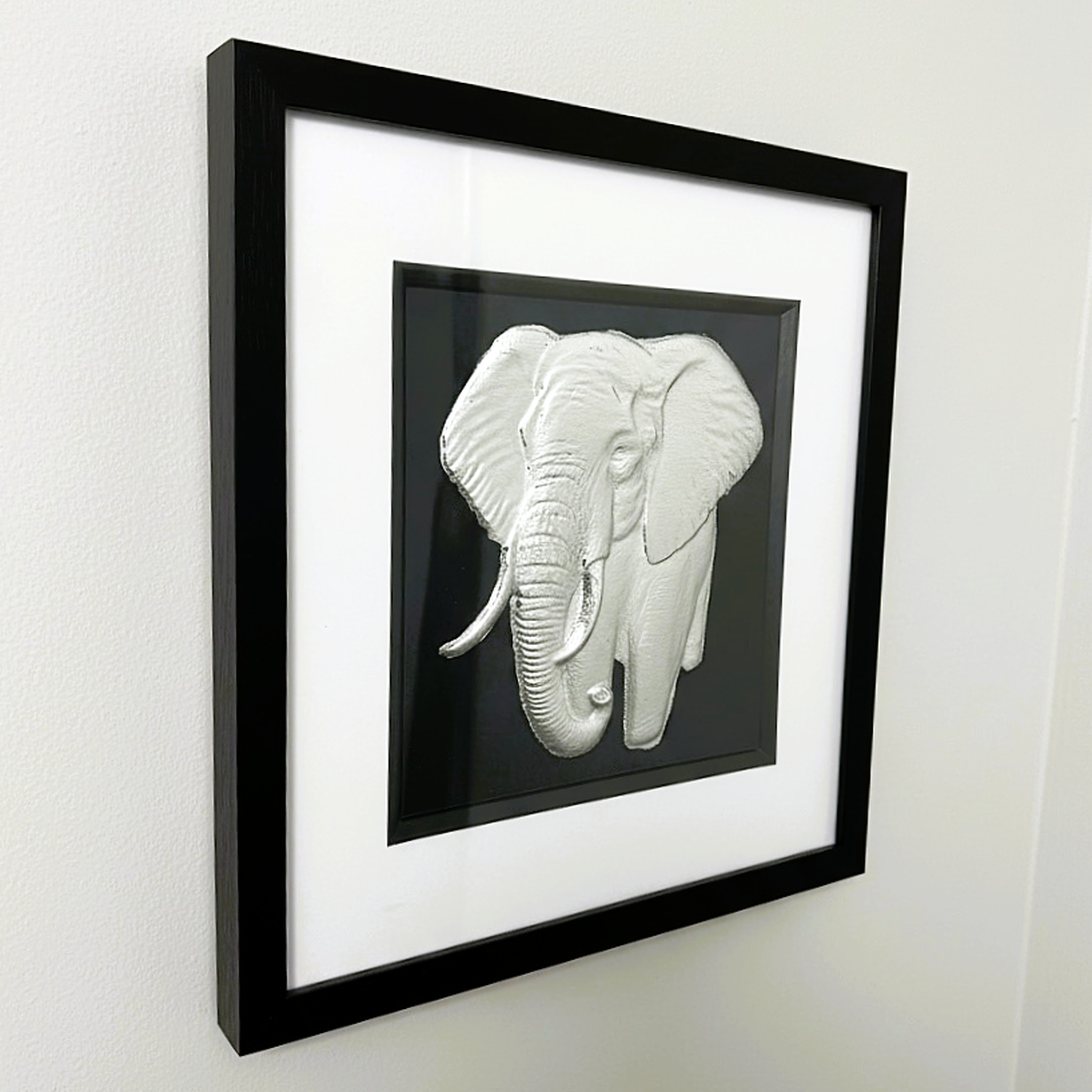 Framed silver elephant wall art shown from an angled wall view