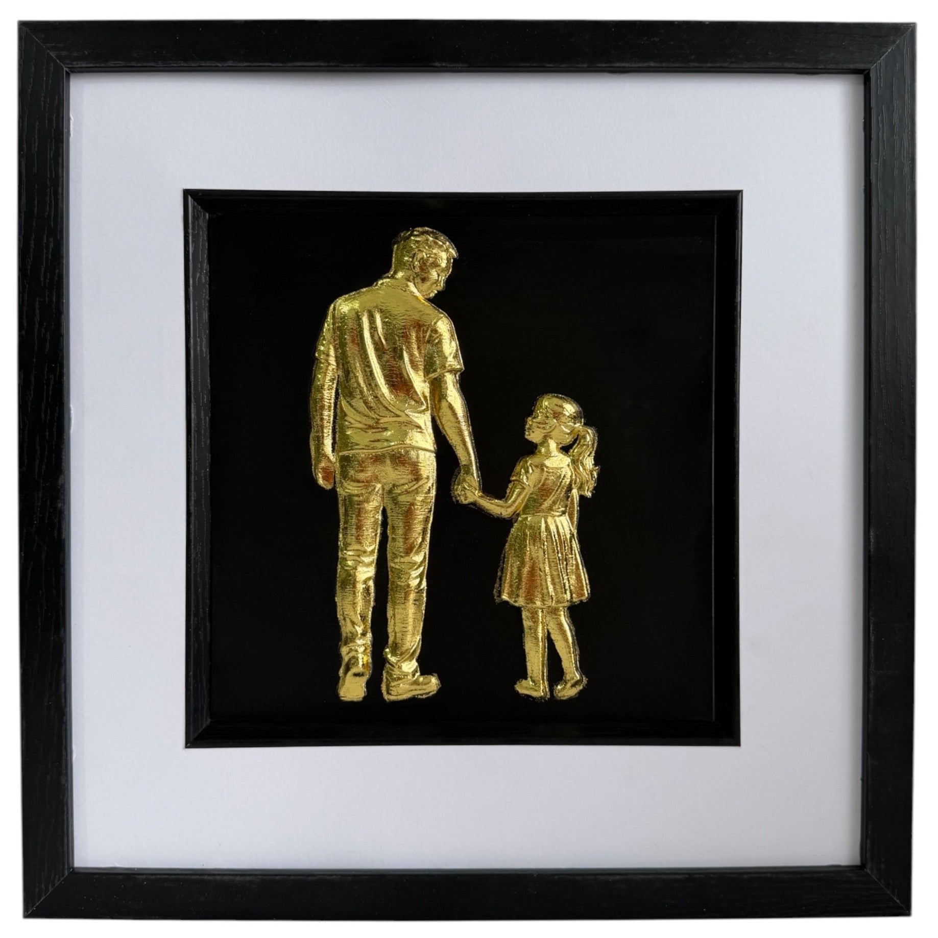 Framed gold leaf father and daughter wall art featuring a parent and child holding hands on a black background with a white mount and black frame.