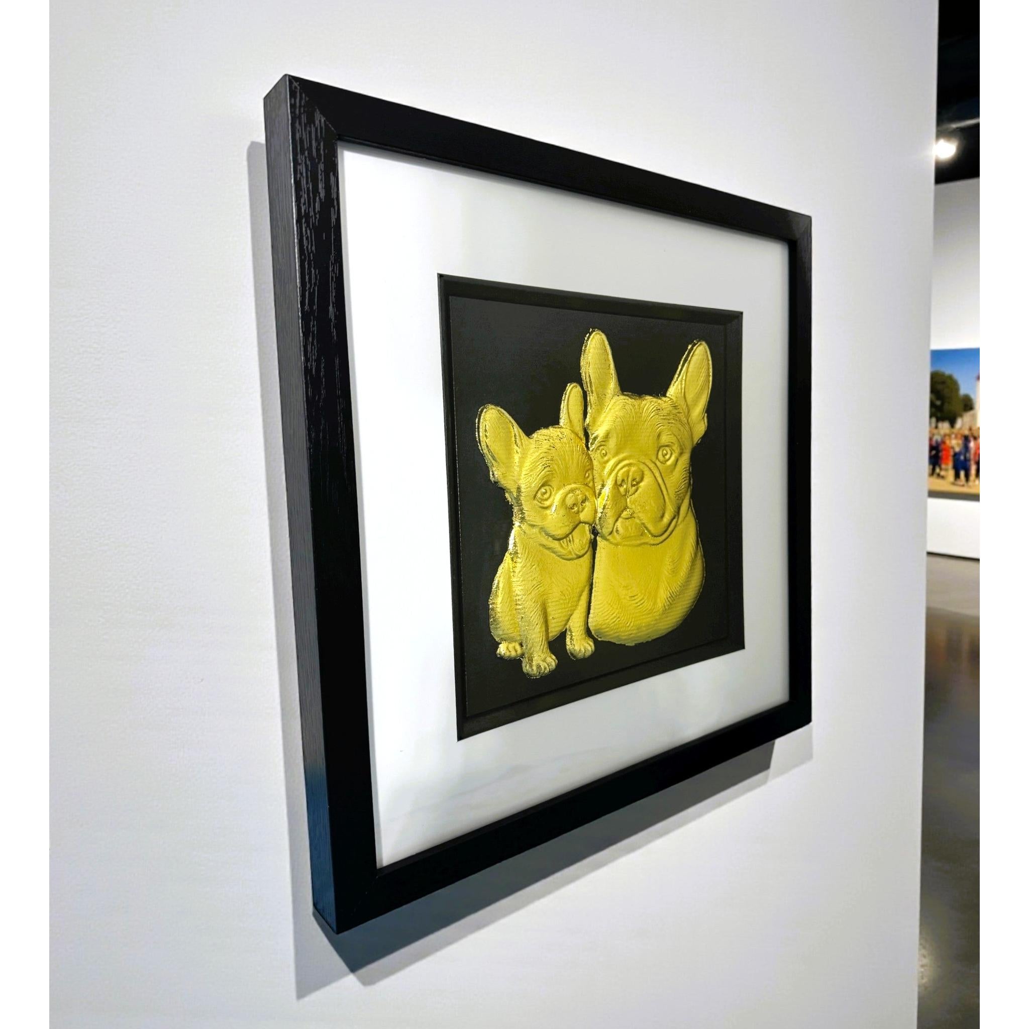 French Bulldog mother and puppy framed wall art in gold leaf mounted on a wall, with black wooden frame, white mount, and black background
