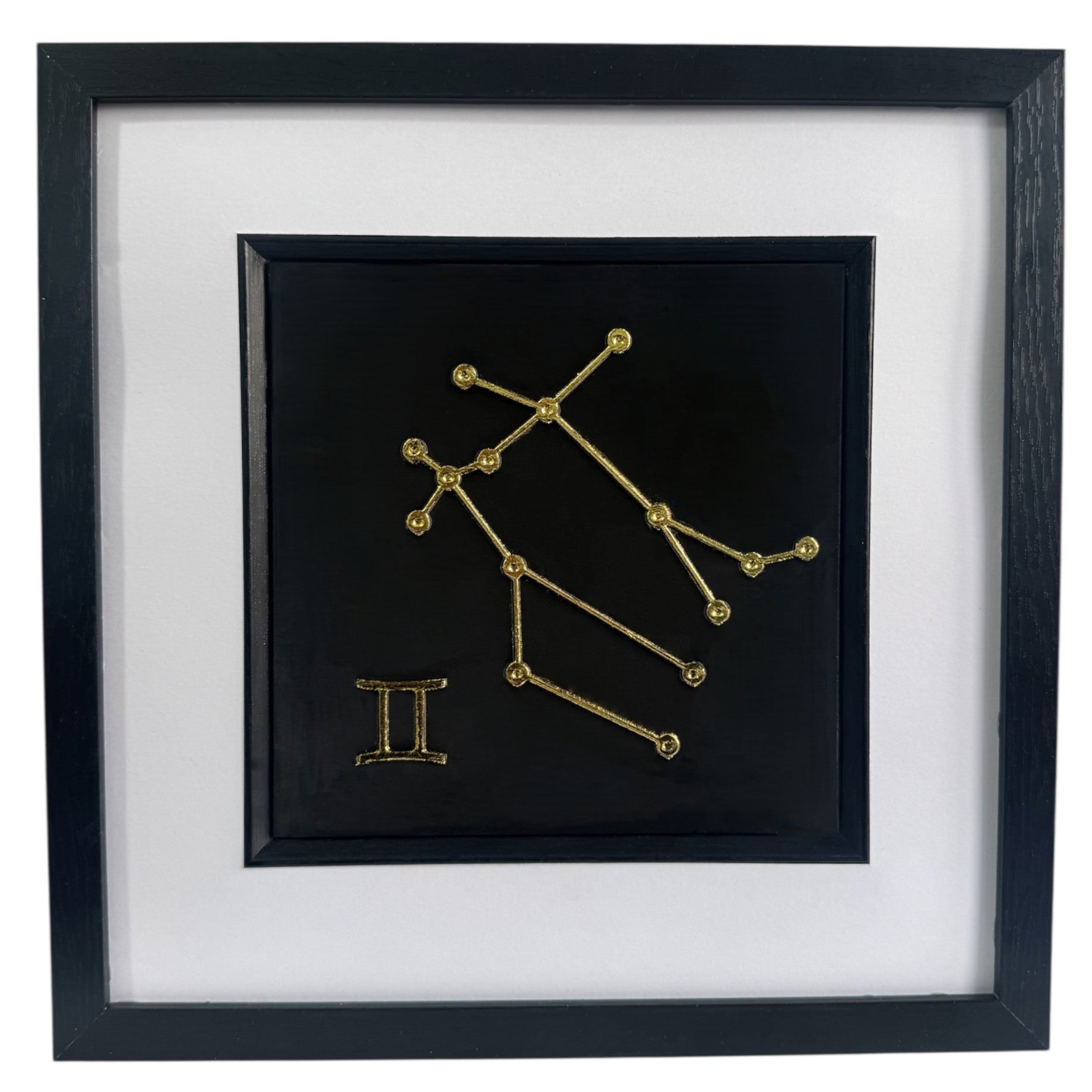 Framed Gemini constellation wall art in gold leaf with star pattern and zodiac symbol, centred on a black background with white mount and black frame