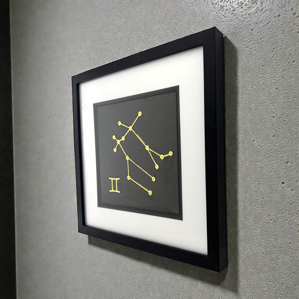 Framed Gemini constellation wall art in gold leaf mounted on a wall, shown at an angle highlighting the depth and clean presentation