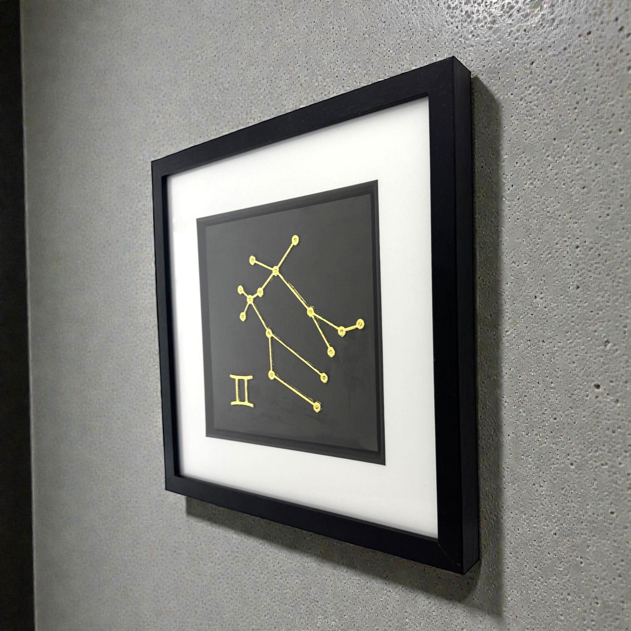 Framed Gemini constellation wall art in gold leaf mounted on a wall, shown at an angle highlighting the depth and clean presentation
