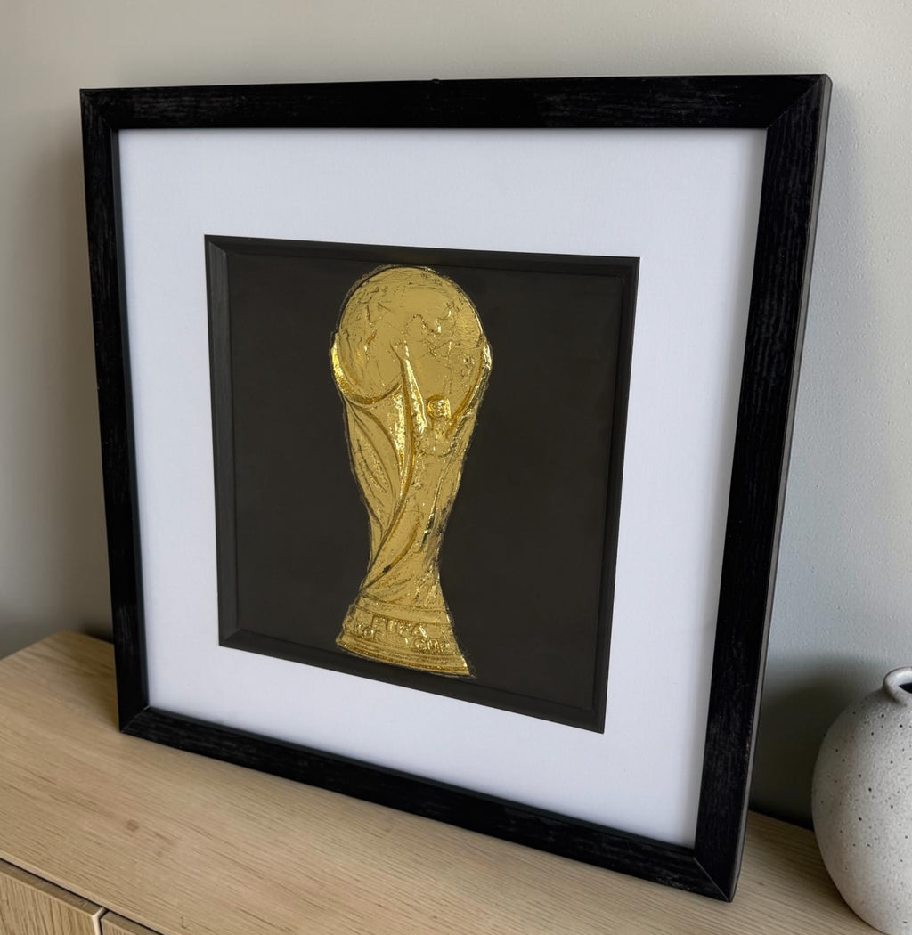 Gold football trophy framed wall art styled on a light wood sideboard beside a neutral vase.