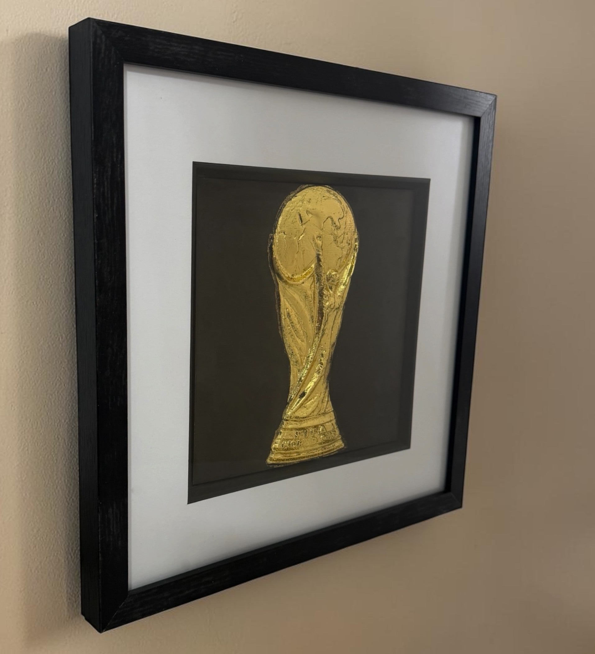 Angled view of framed gold football trophy relief showing the deep black box frame and glass front.