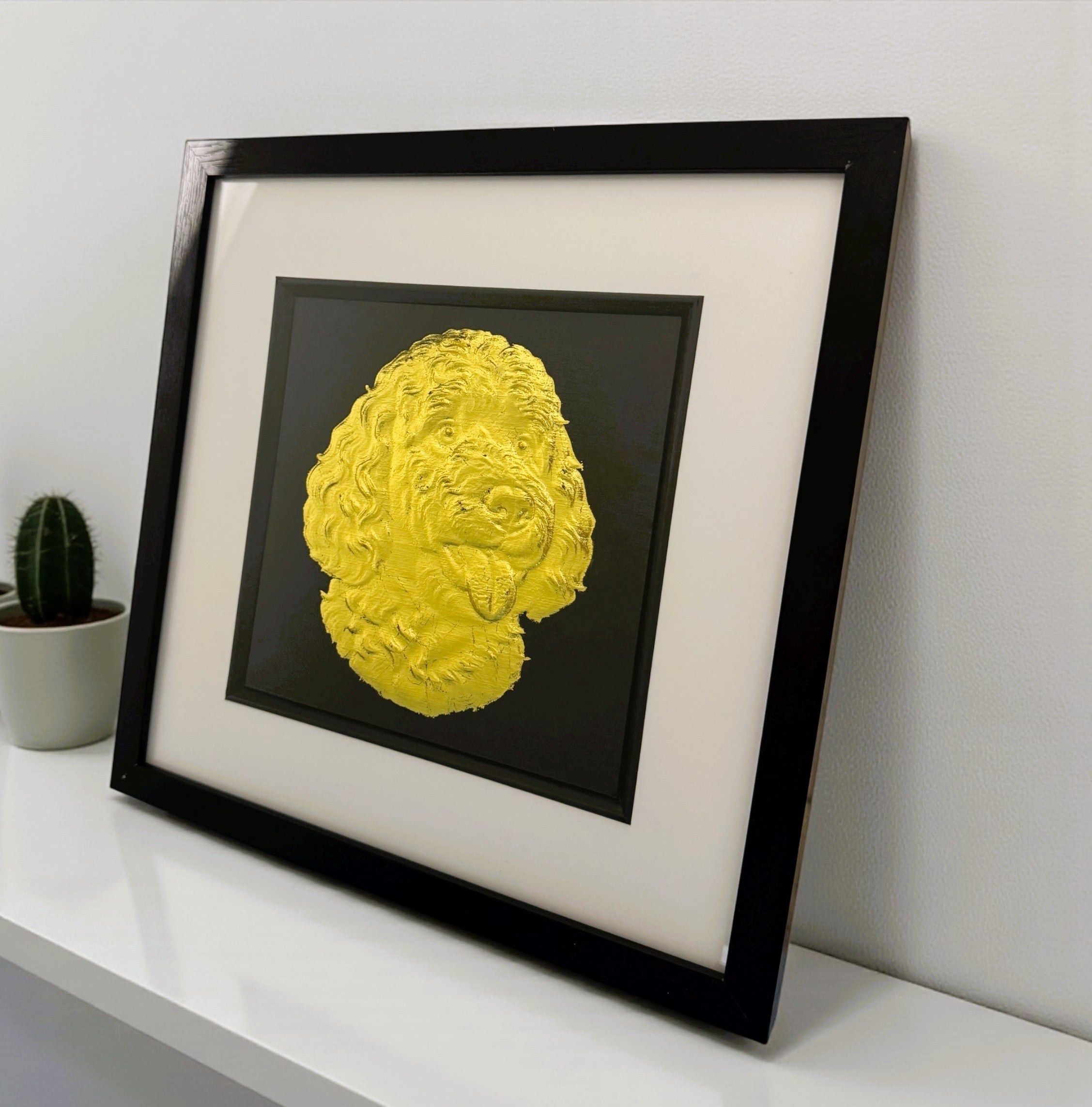 goldendooldle dog portrain gold leaf in a black frame standing on a white desk and leaning against a wall