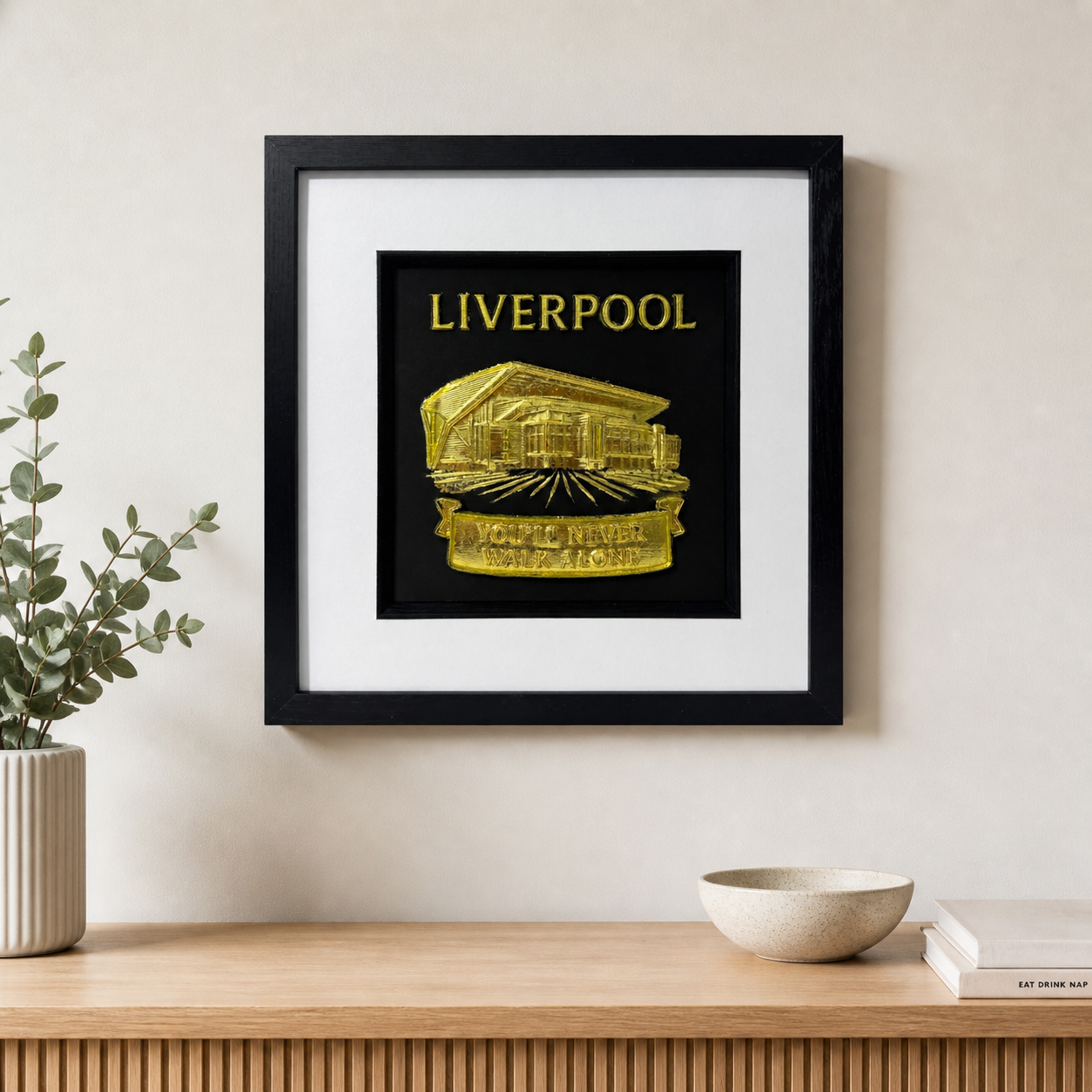 Lifestyle photo of Liverpool FC Anfield wall art displayed on a neutral wall above a wooden sideboard with home decor.
