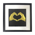 Framed love heart hands wall art in gold leaf relief, centred on a black background with white mount and black frame
