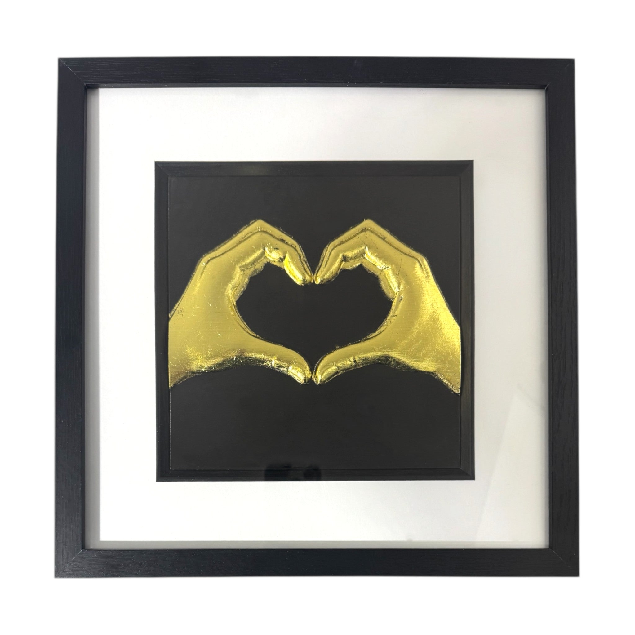Framed love heart hands wall art in gold leaf relief, centred on a black background with white mount and black frame