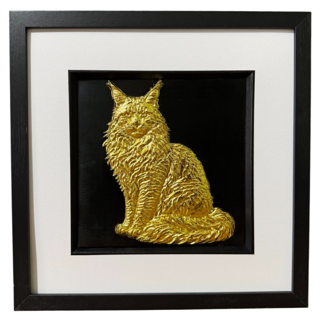 Framed Maine Coon cat wall art, gold relief of a sitting long-haired cat with tufted ears, ruff and plumed tail, on a black background in a black frame with white mount