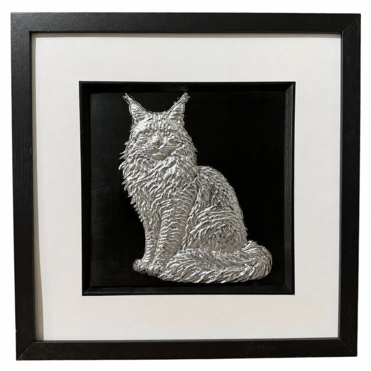 Framed Maine Coon cat wall art, silver relief of a sitting long-haired cat with tufted ears and a bushy tail round its paws, on a black background in a black frame with white mount