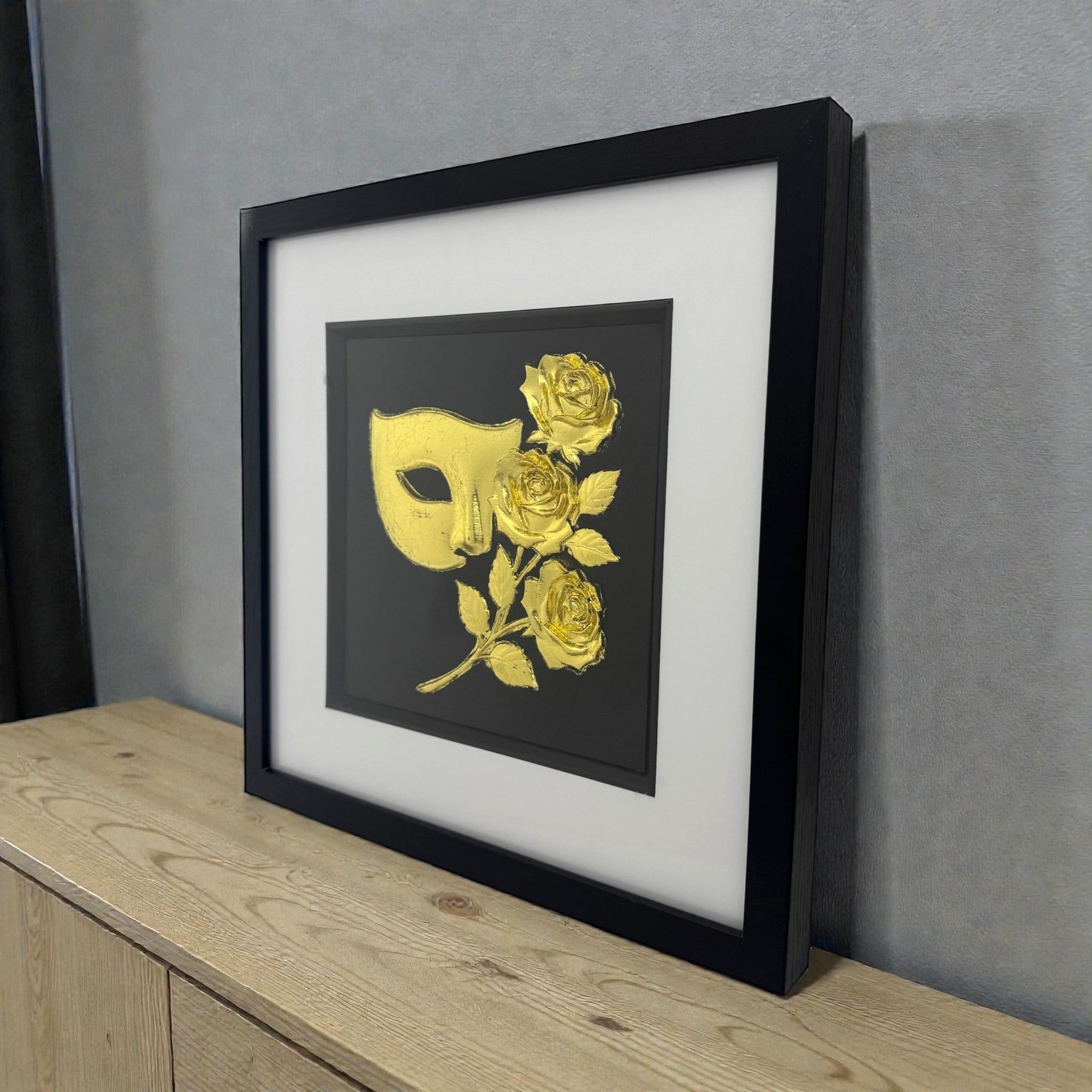 Masquerade mask and roses wall art in gold leaf styled on a light wood cabinet in a black frame with white mount