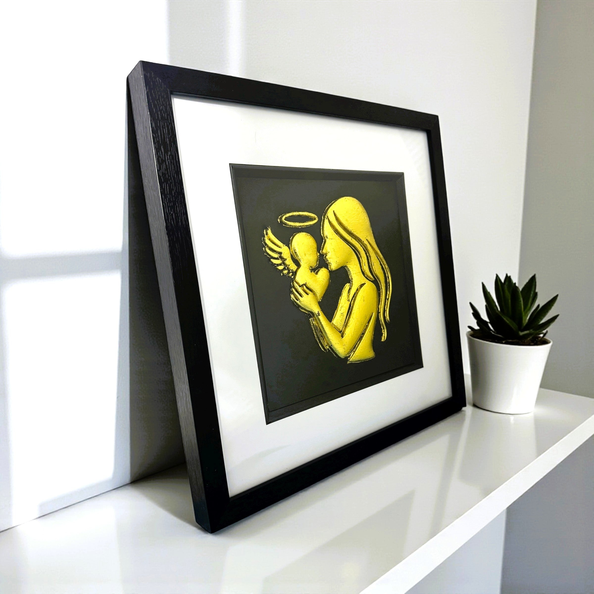 Angled desk view of mother and baby angel framed wall art with silver leaf finish