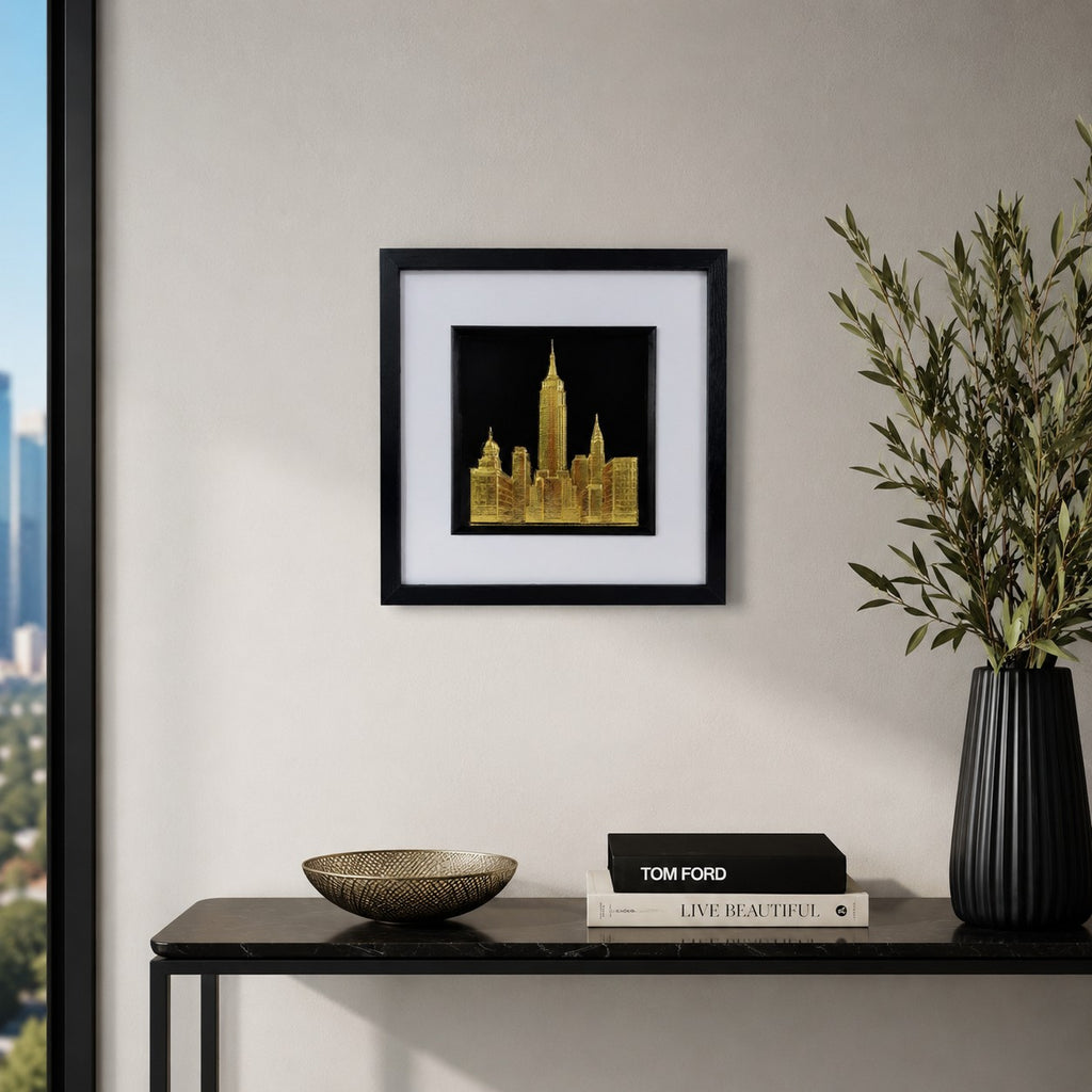 Gold New York cityscape artwork styled above a black console table with books, bowl, plant and city-view room setting.