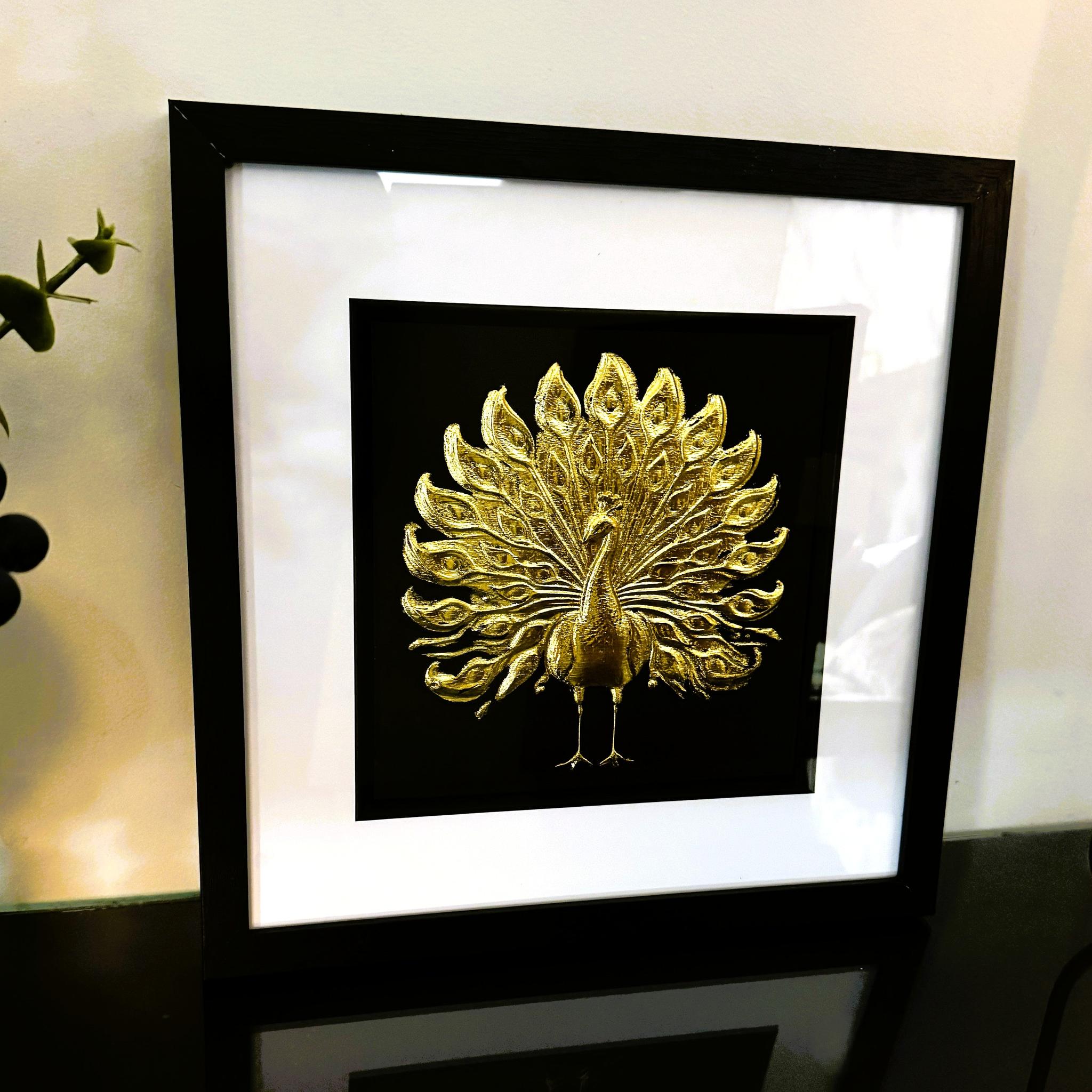 Gold peacock wall art framed in black with white mount on a light wall