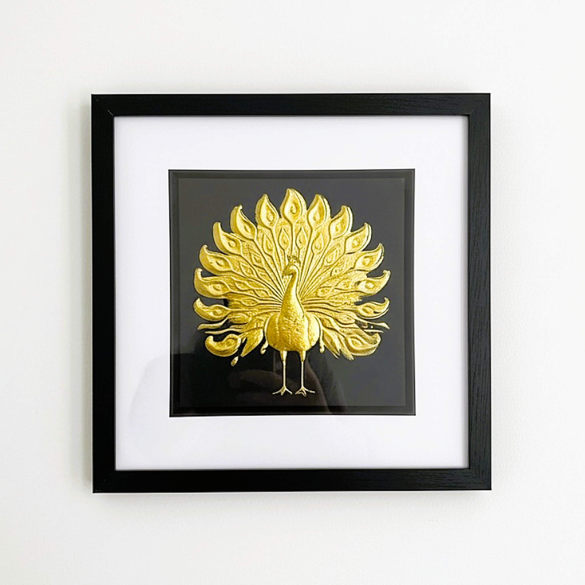 Gold peacock artwork framed and centred against a white wall