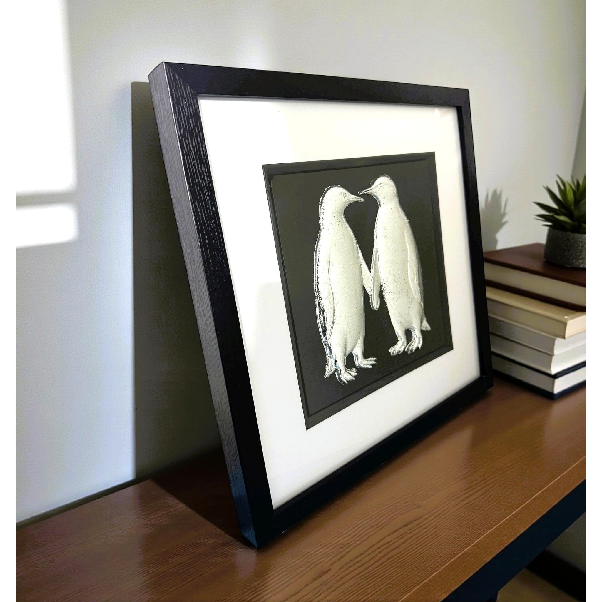 Silver penguin couple framed wall art viewed at an angle on a shelf
