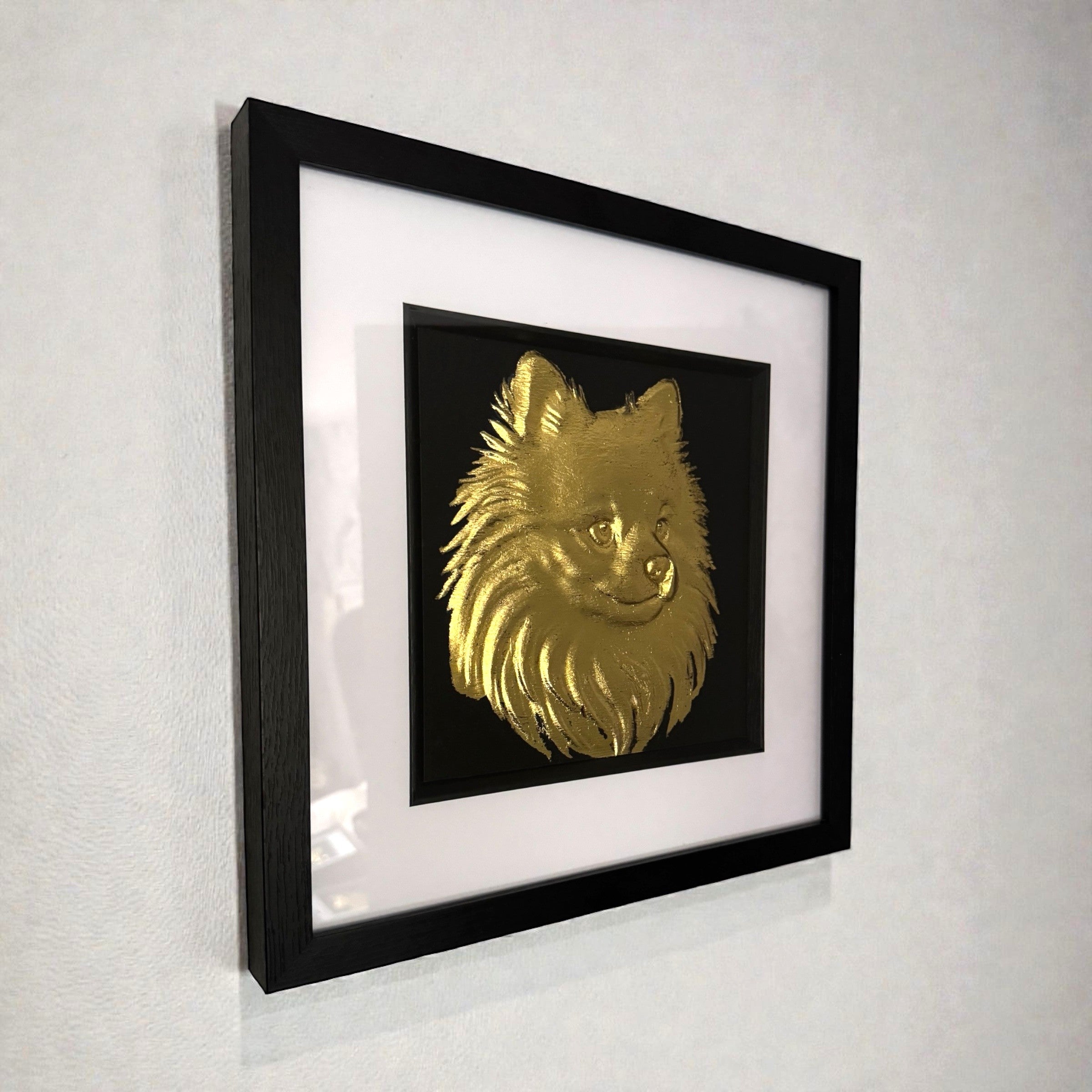Pomeranian gold leaf framed wall art shown mounted on a wall at a slight angle with black frame and white mount