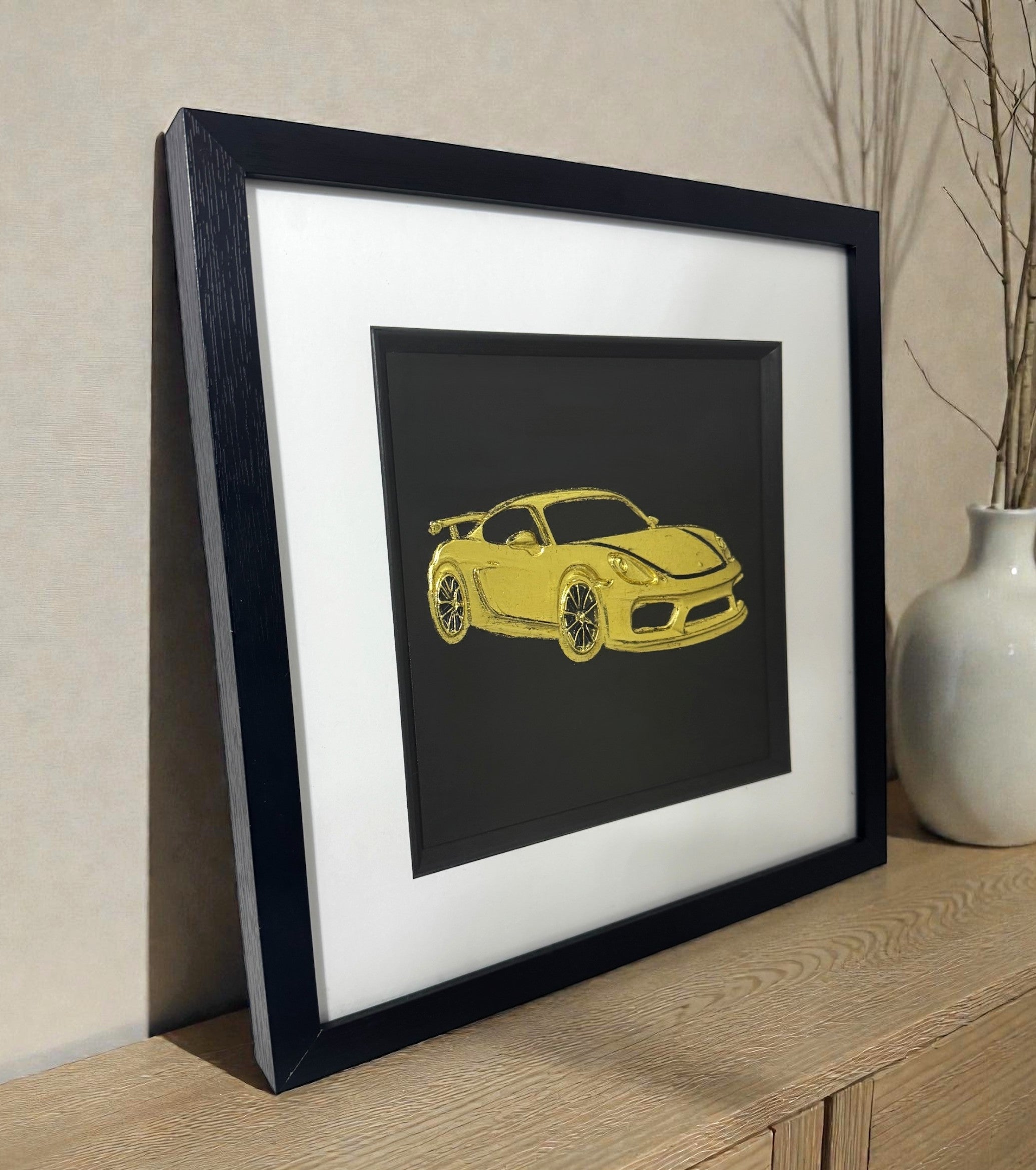 Gold leaf Porsche GT4 wall art displayed on a wooden sideboard, black frame with white mount, 33 x 33 cm