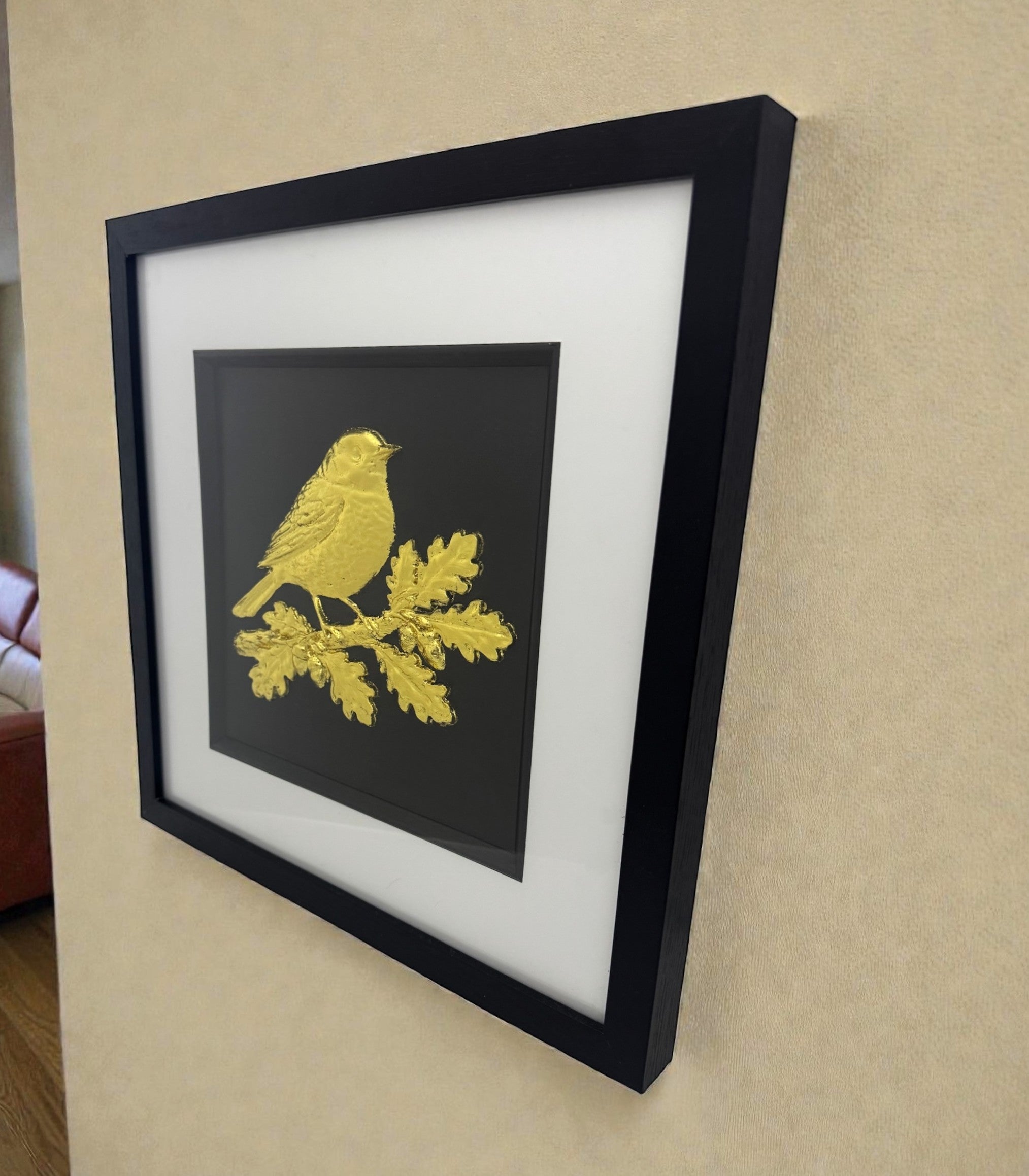 Gold leaf robin wall art perched on an oak branch hung on a wall, framed